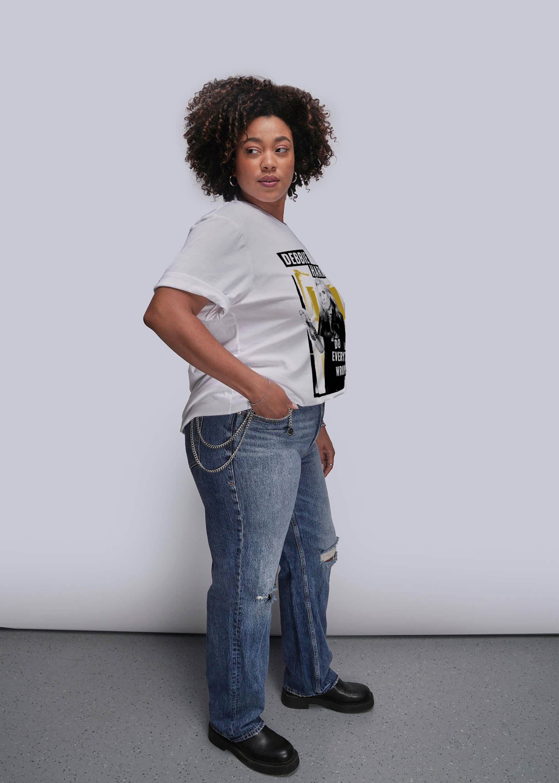 1X=Person wearing a white t-shirt with graphic design and blue jeans against a plain background