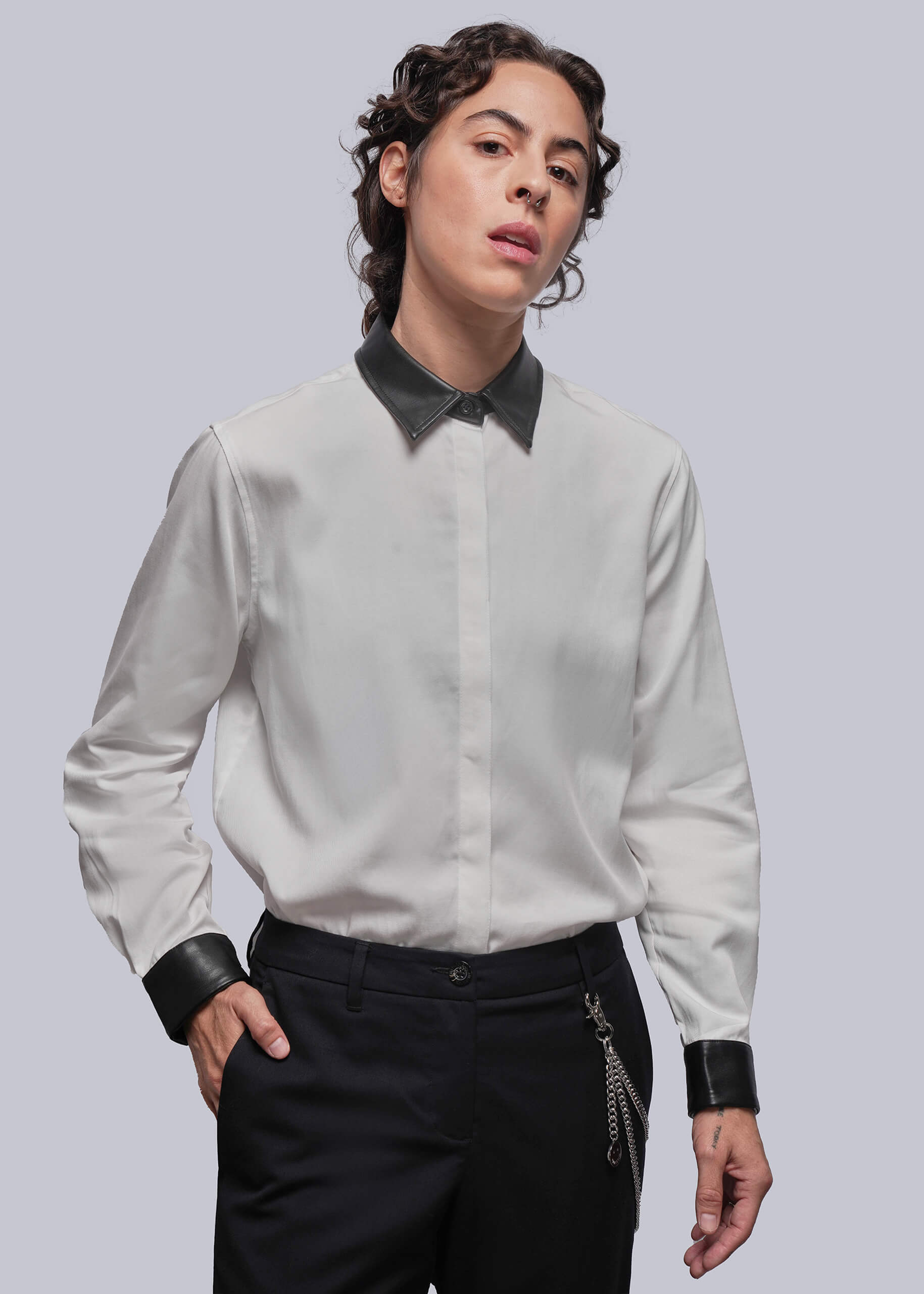Person wearing a white shirt with black collar and cuffs against a light gray background
