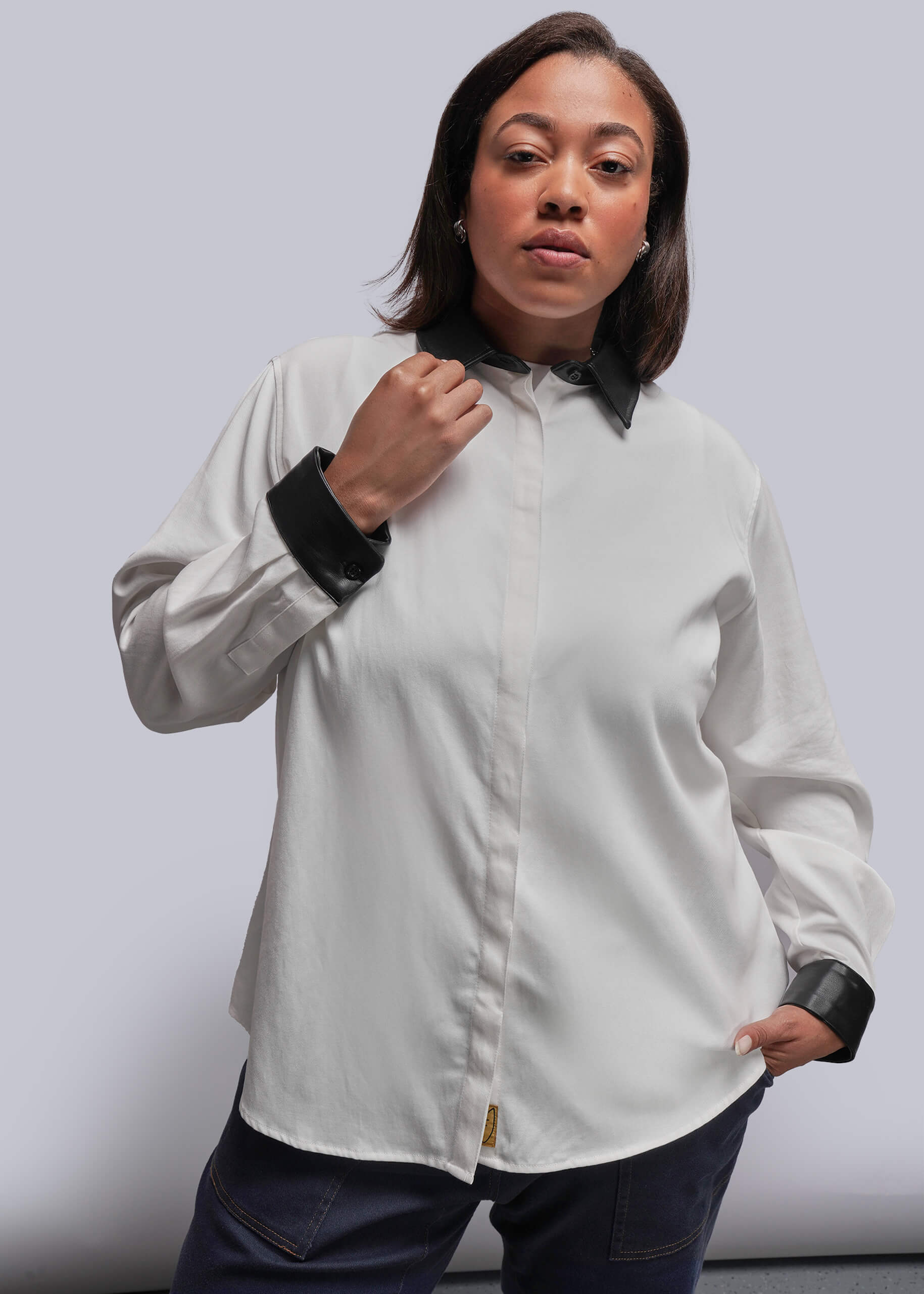 1X=Person wearing a white button-up shirt with black cuffs and collar against a plain background