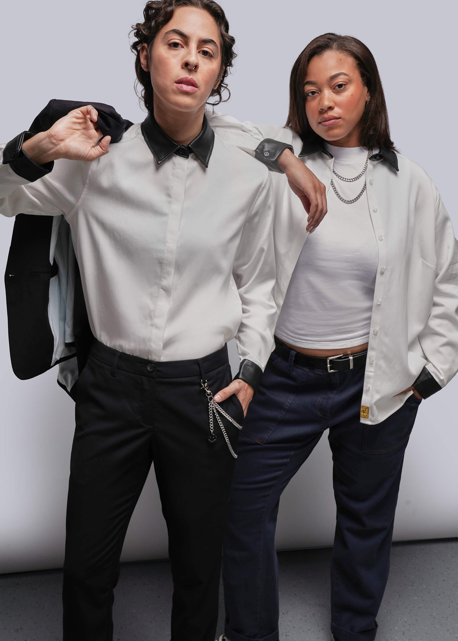 Two people wearing white shirts and dark pants against a plain background