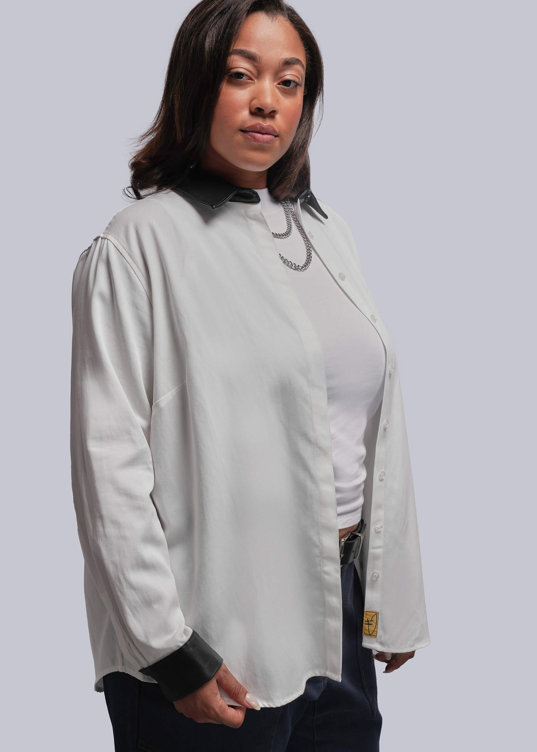 1X=Person wearing a white long-sleeve button up unbuttoned over white top against a plain background.