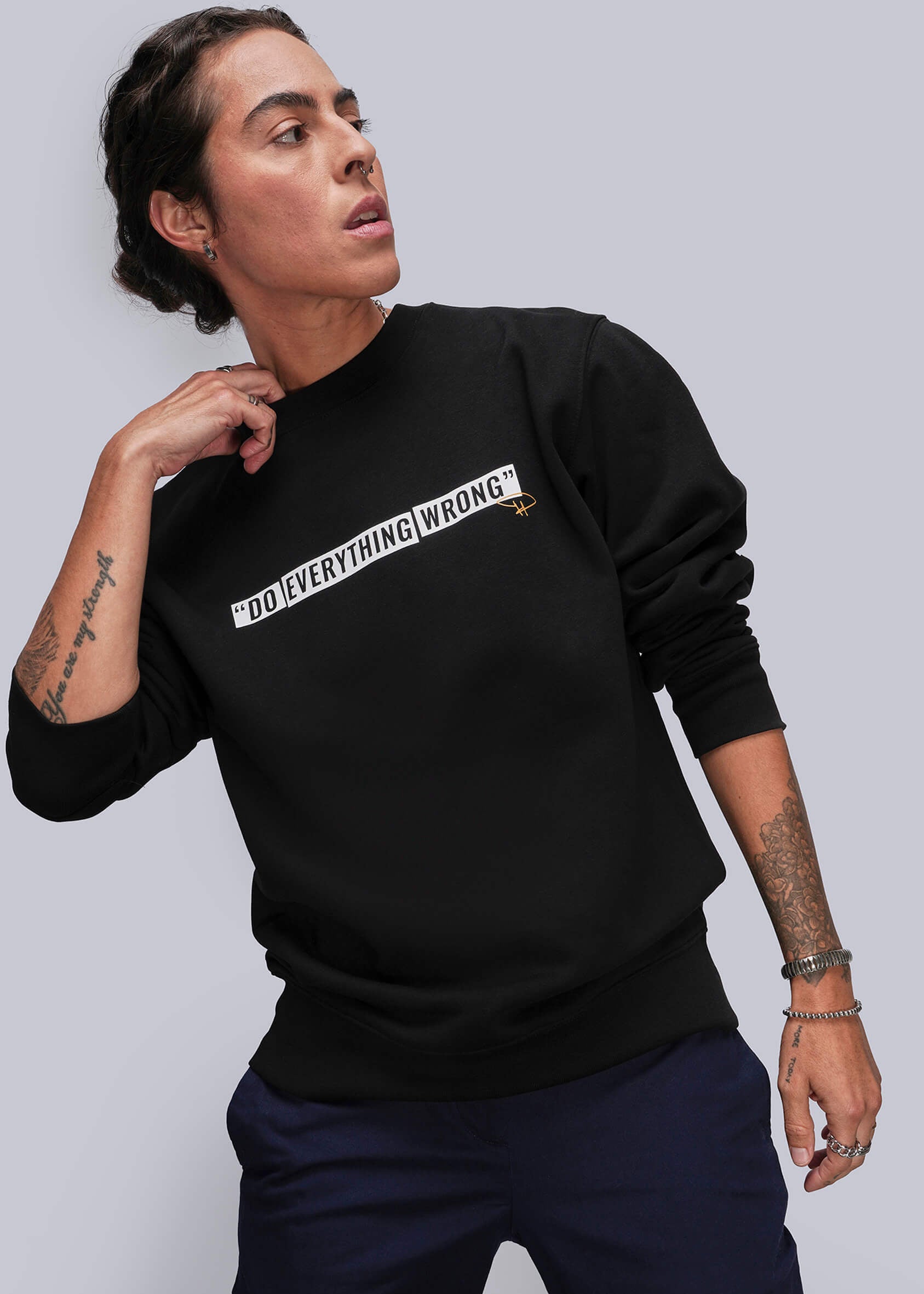 Person wearing a black sweatshirt with text, standing against a plain background