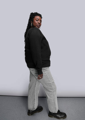 1X=Person wearing a black crew neck and light gray pants against a white background