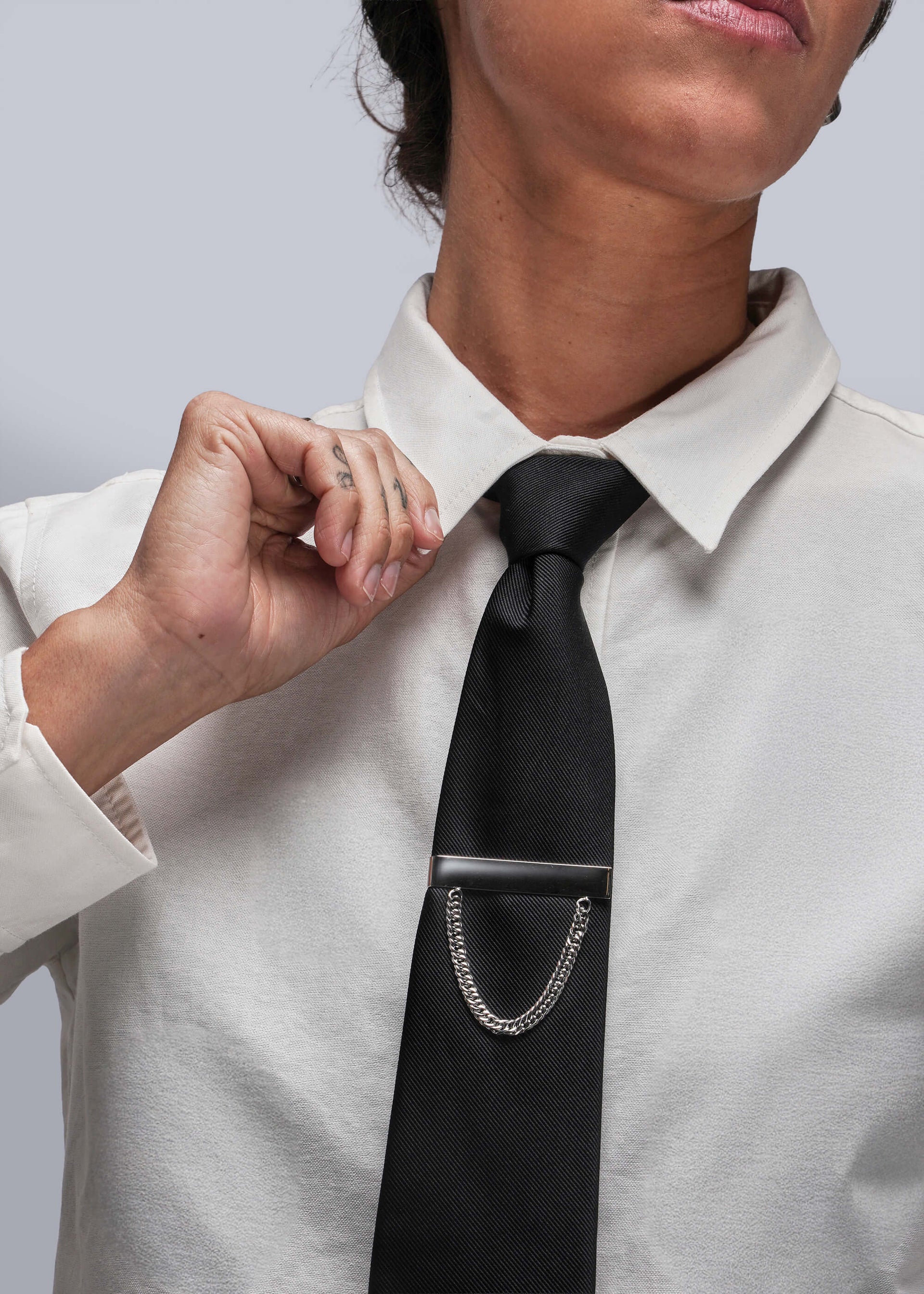 Person adjusting a black tie with a silver tie clip on a white shirt against a light gray background
