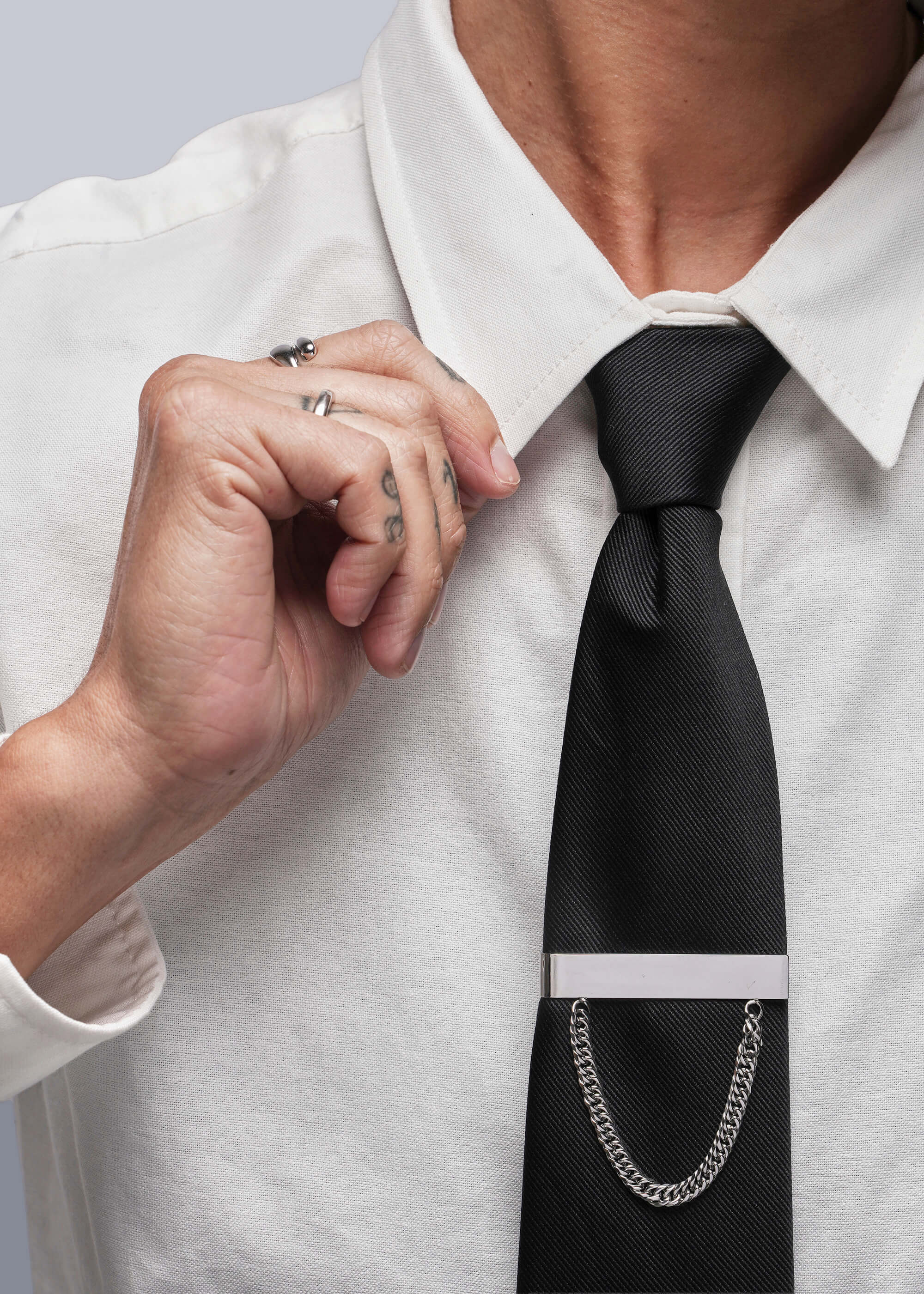 Person adjusting a black tie with a silver tie clip on a white shirt.