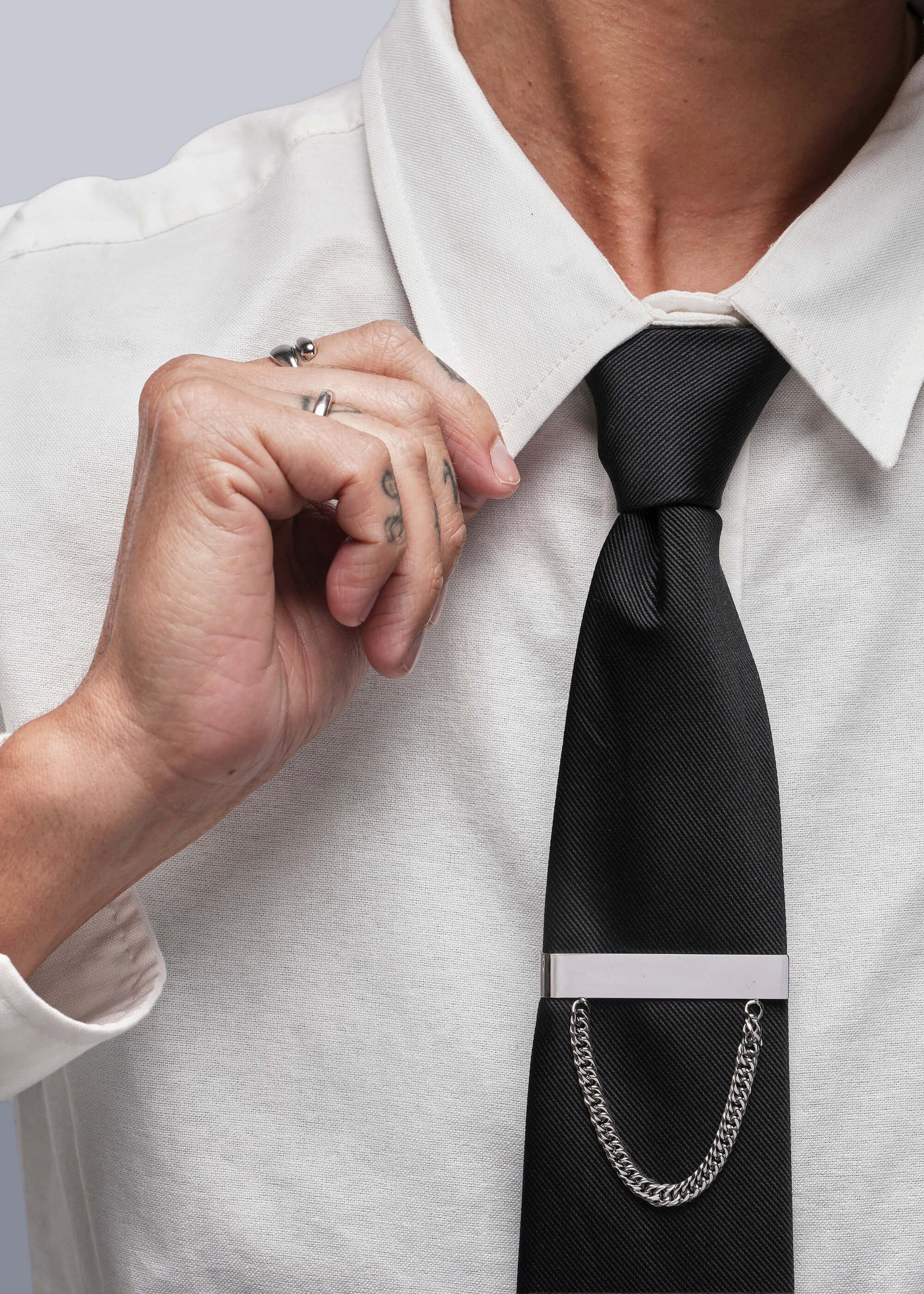 Person adjusting a black tie with a silver tie clip on a white shirt.