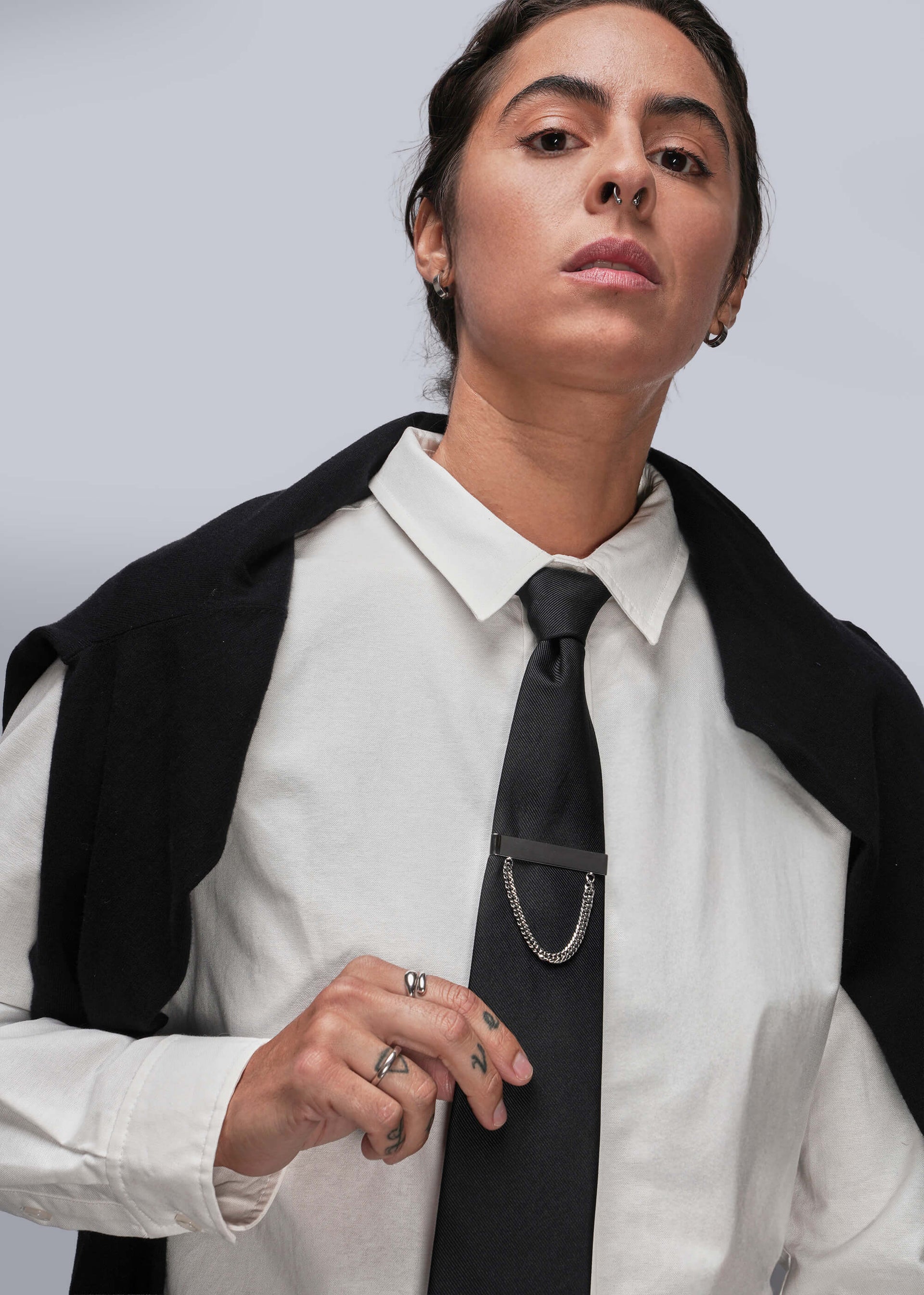 Person wearing a white shirt, black tie with tie clip, and black jacket against a light gray background