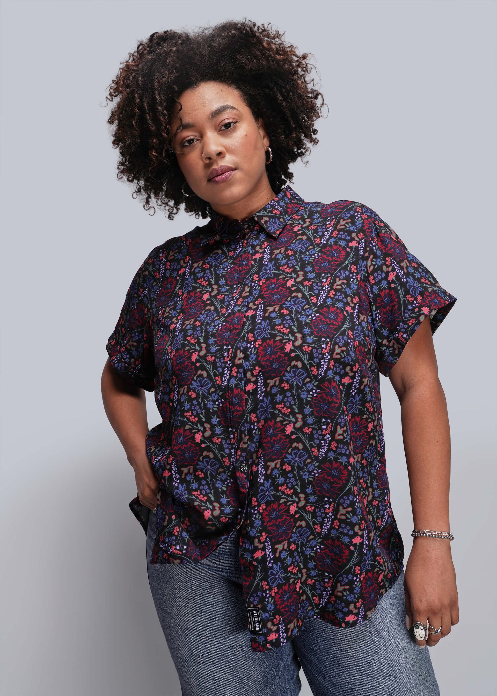 1X=Person wearing a patterned shirt and jeans against a plain background