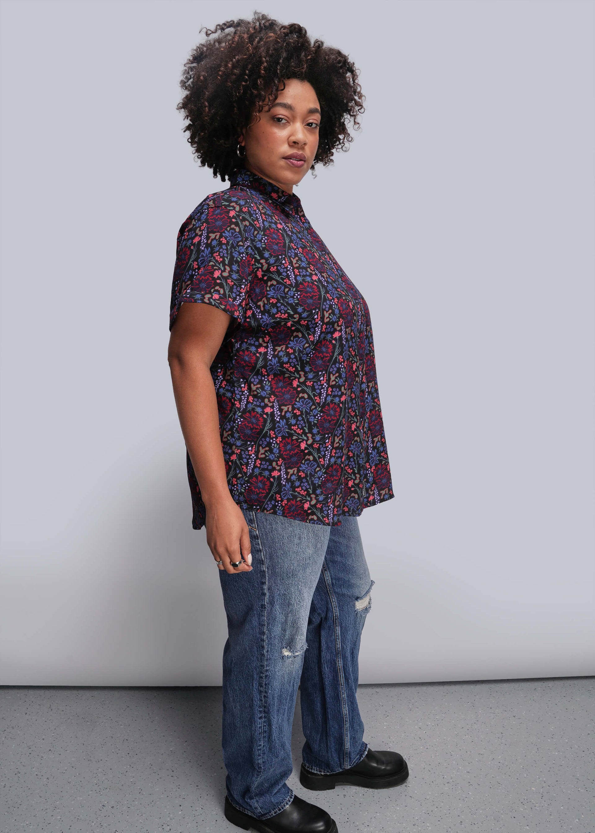 1X=Person wearing a patterned shirt and jeans against a plain background