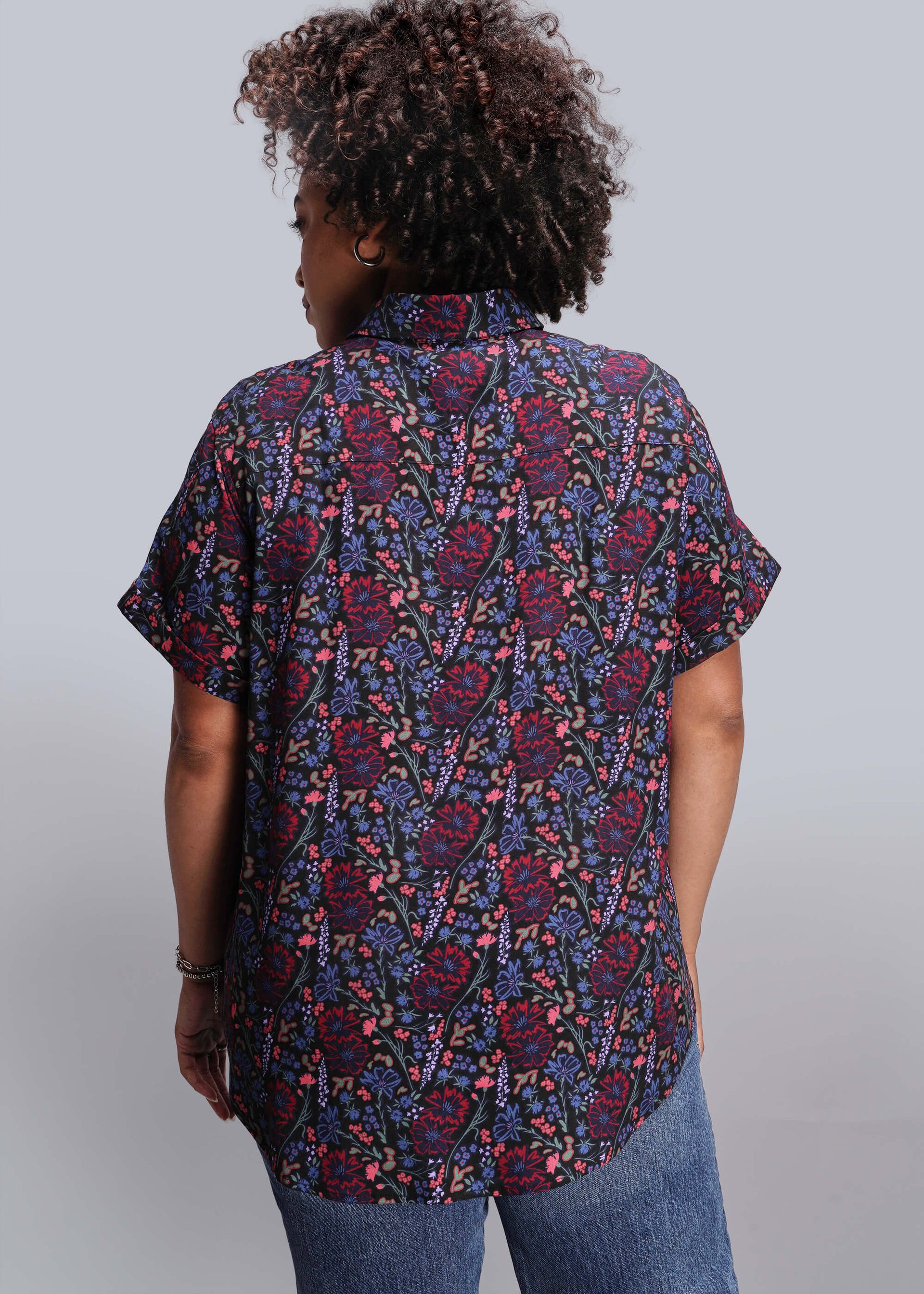 1X=Person wearing a patterned shirt with short sleeves on a plain background