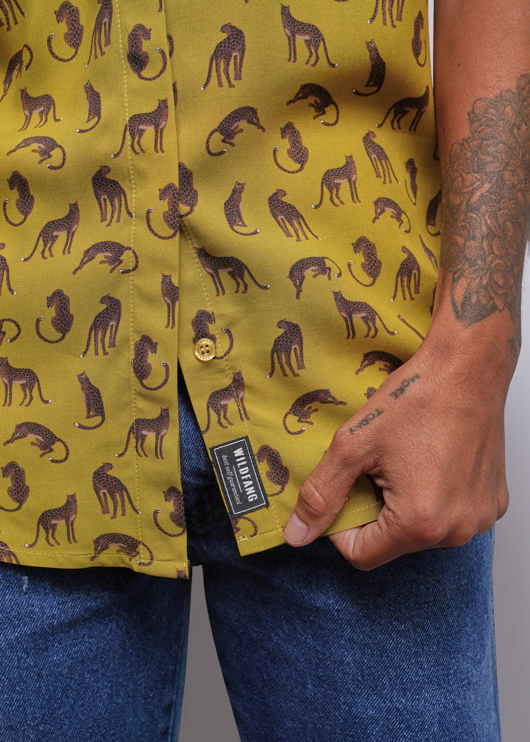 S=Close-up of a person wearing a mustard yellow button-up shirt with a repeating dark cat silhouette print, paired with blue jeans. The shirt has a visible black brand label reading 'WILDFANG'.