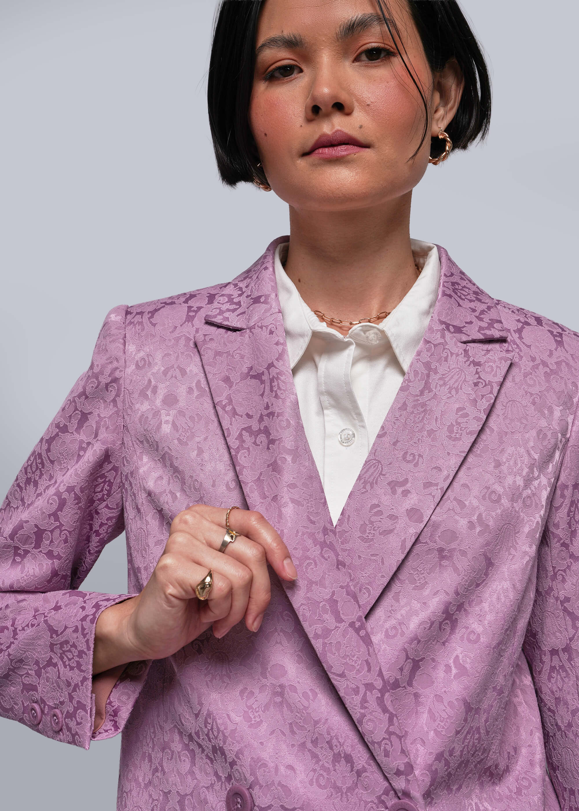 Person wearing a pink floral blazer over a white shirt on a gray background