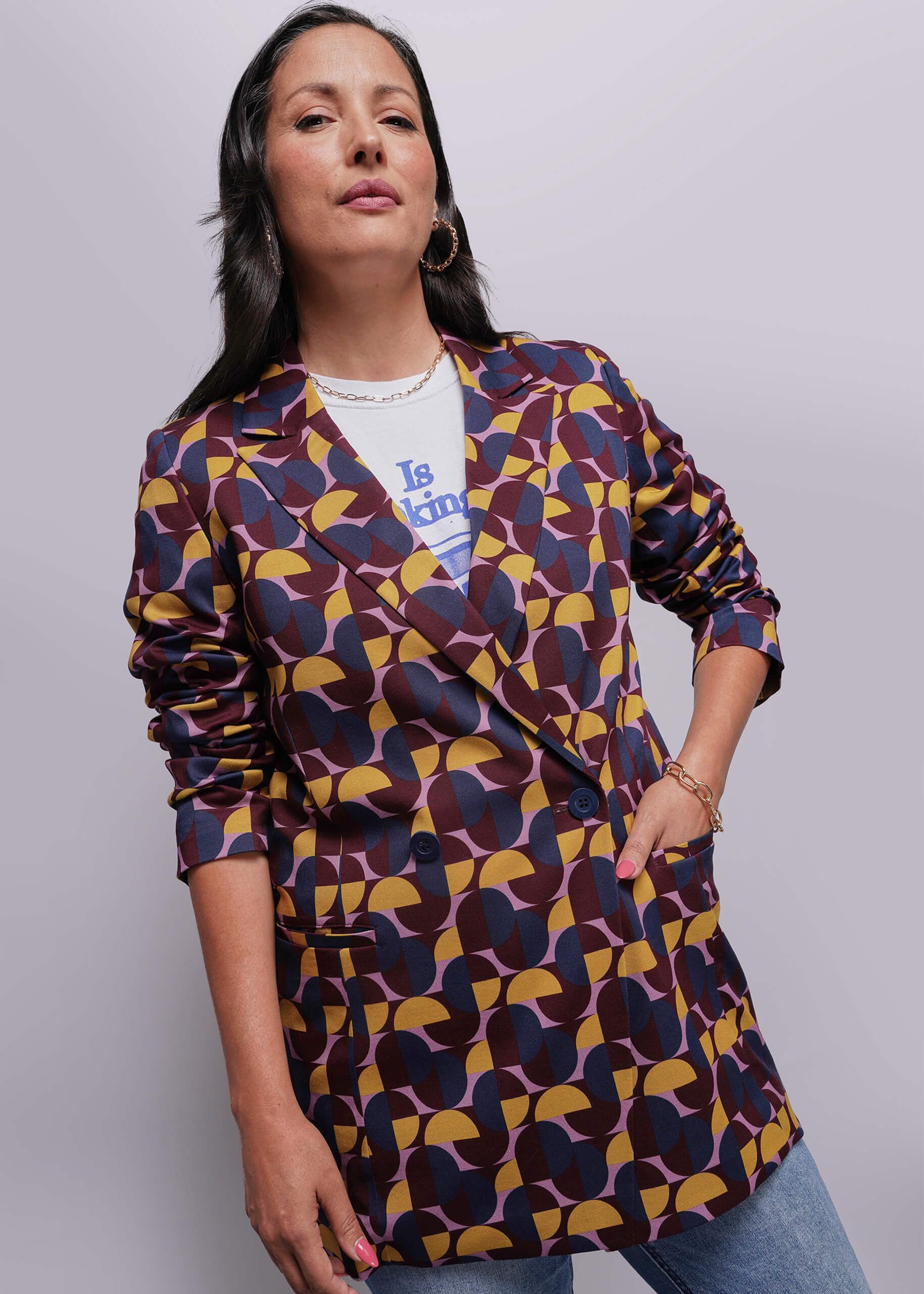 Woman wearing a patterned blazer over a white shirt with text, standing against a plain background