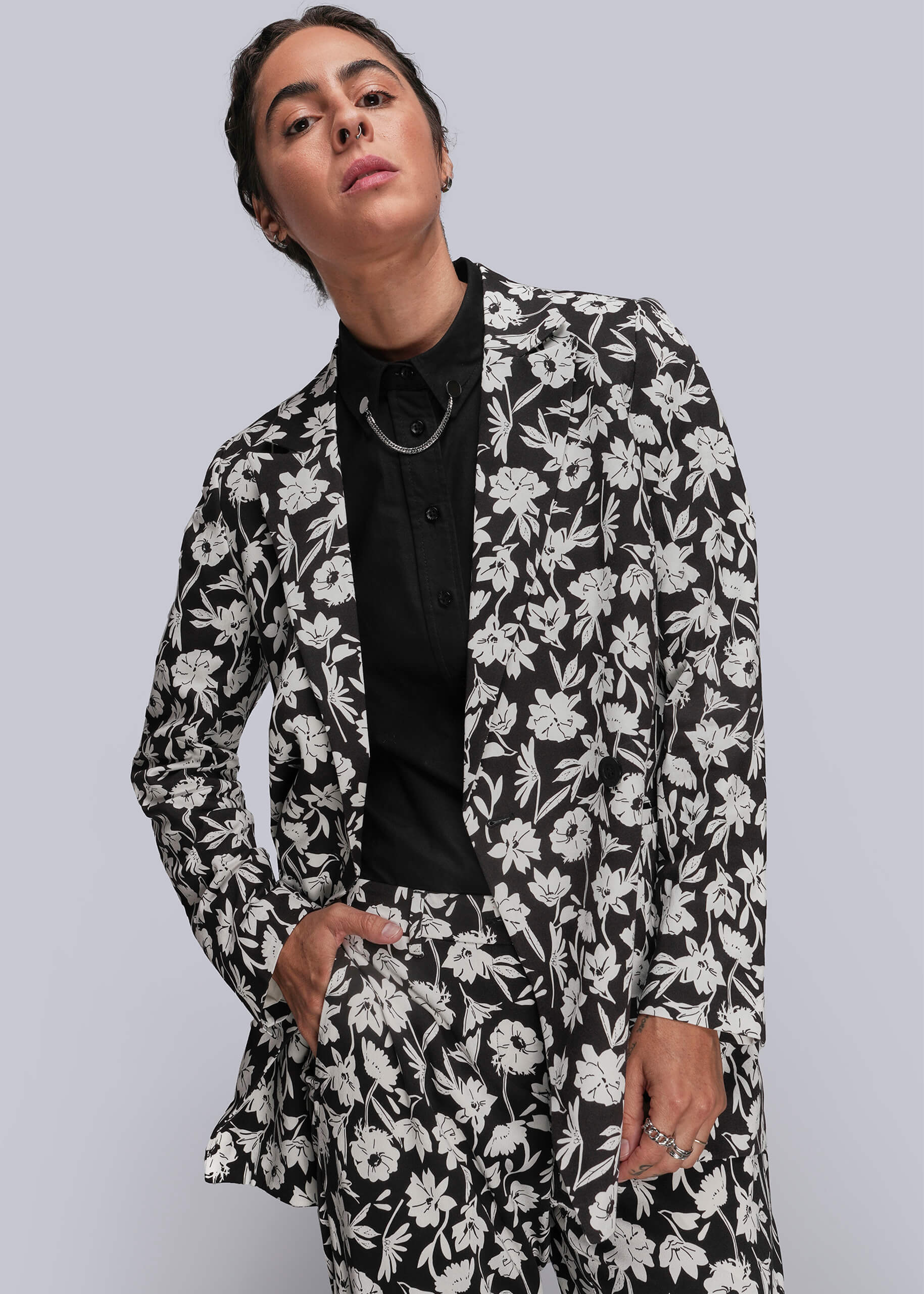 Person wearing a black and white floral suit against a gray background