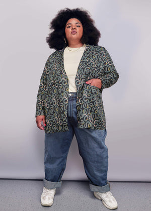 1X=Person wearing a patterned jacket and jeans against a plain background