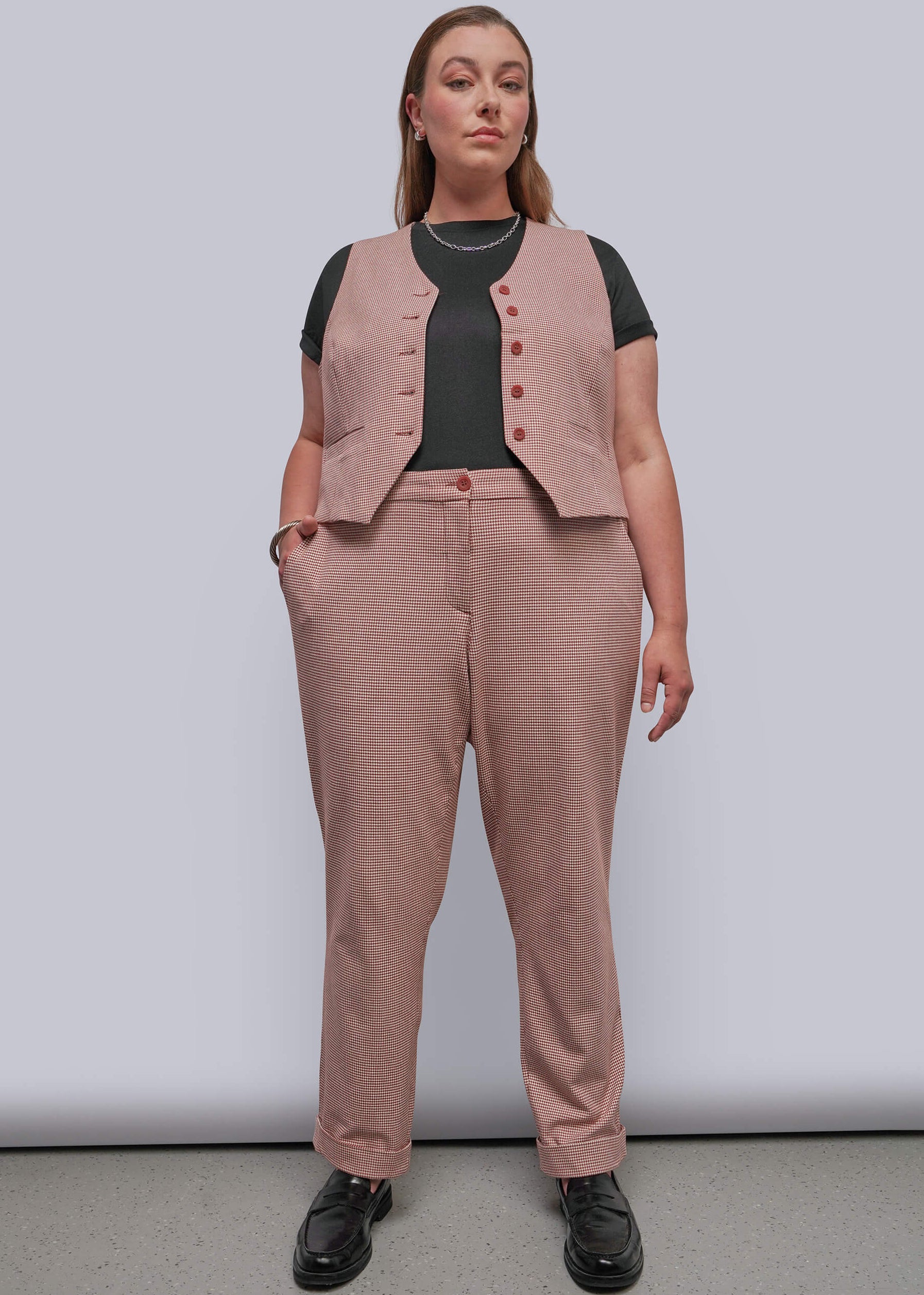 1X=A woman modeling a dusty red button-front vest and matching trousers over a black short-sleeve top, standing against a light gray studio background.