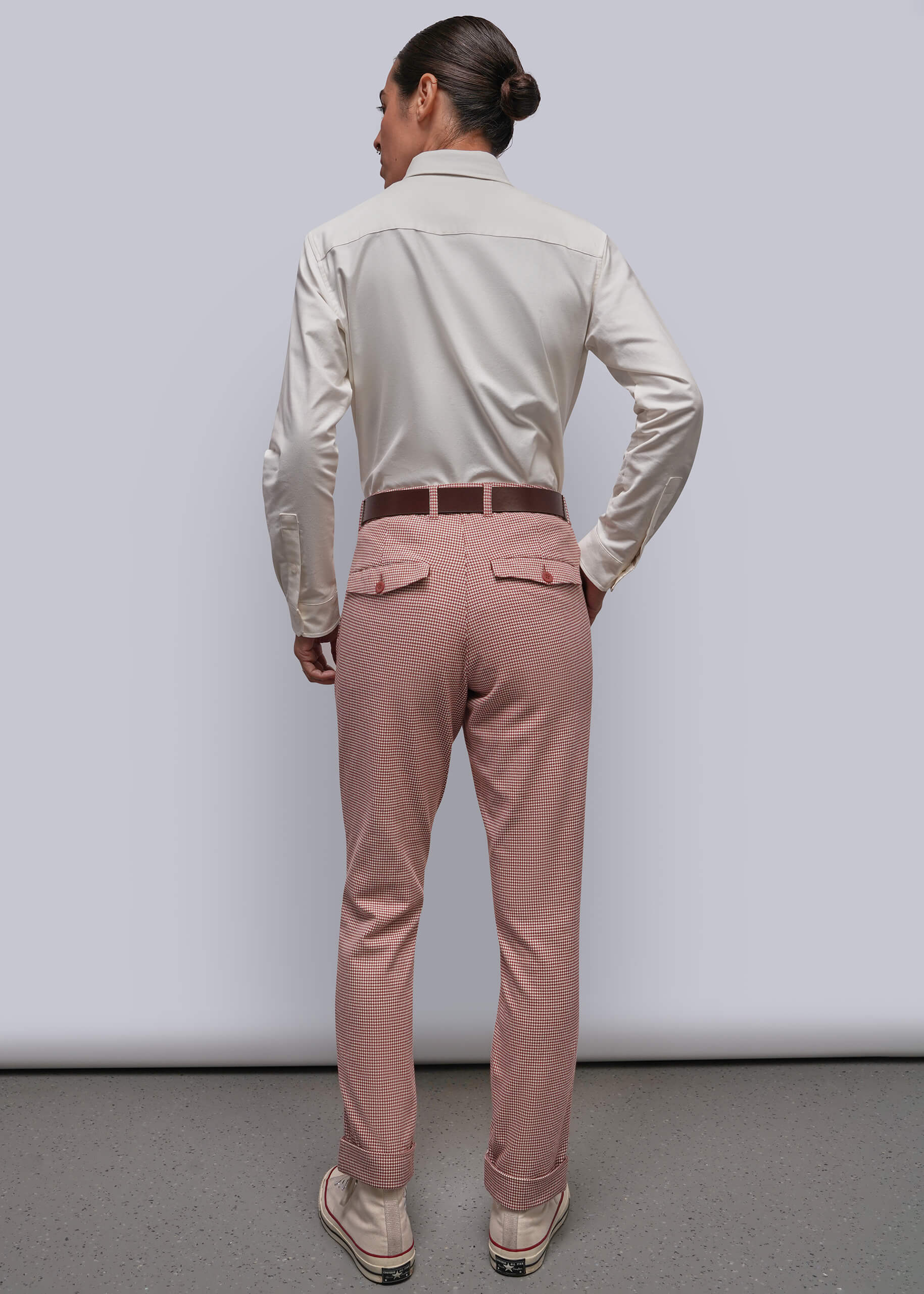 S=A person is shown from behind wearing a light long-sleeve button-down shirt, dusty red patterned trousers, and a brown belt against a plain light gray studio background.