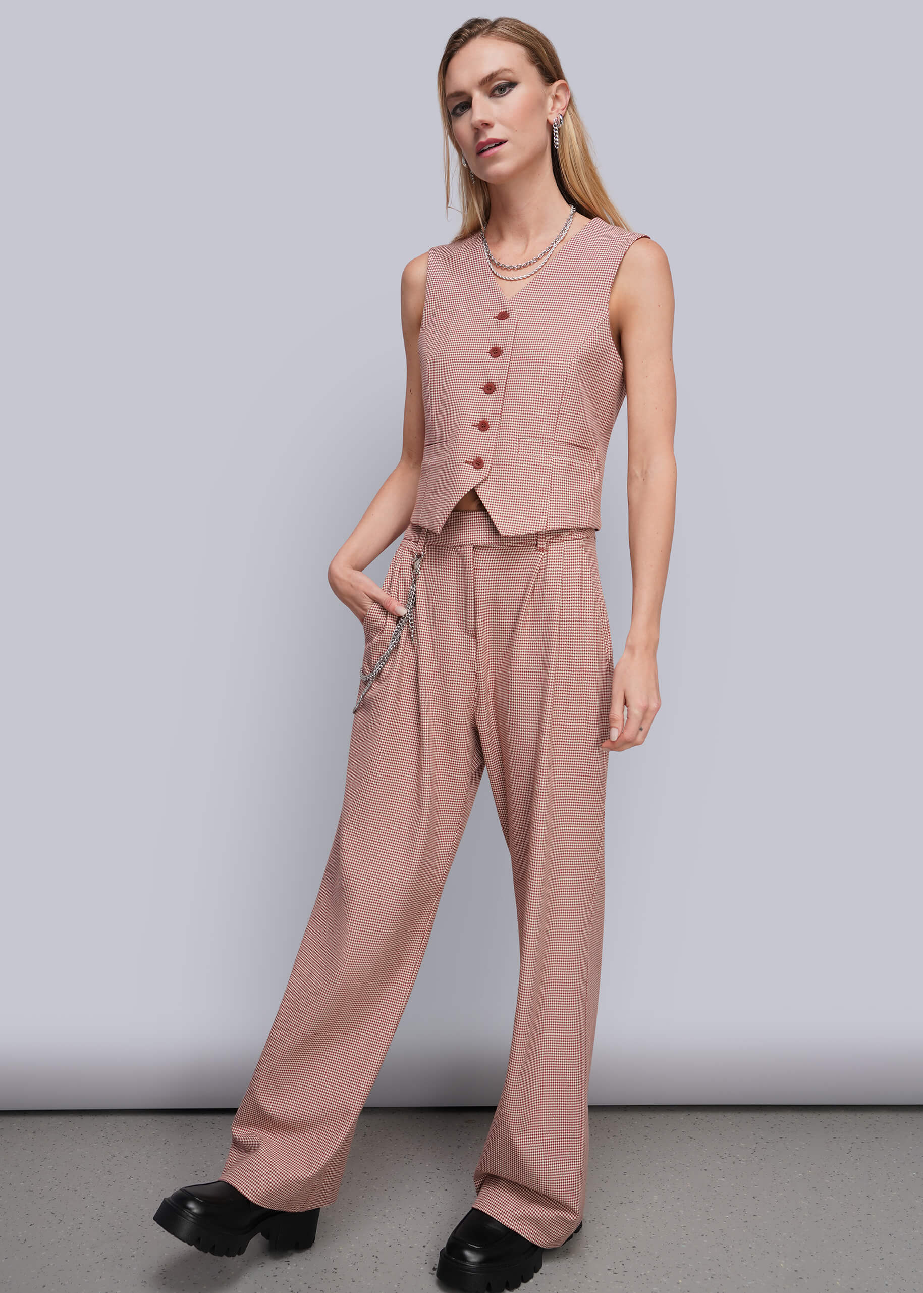 S=A woman modeling a dusty red sleeveless vest and matching wide-leg trousers, styled with black platform shoes against a plain light gray studio background.