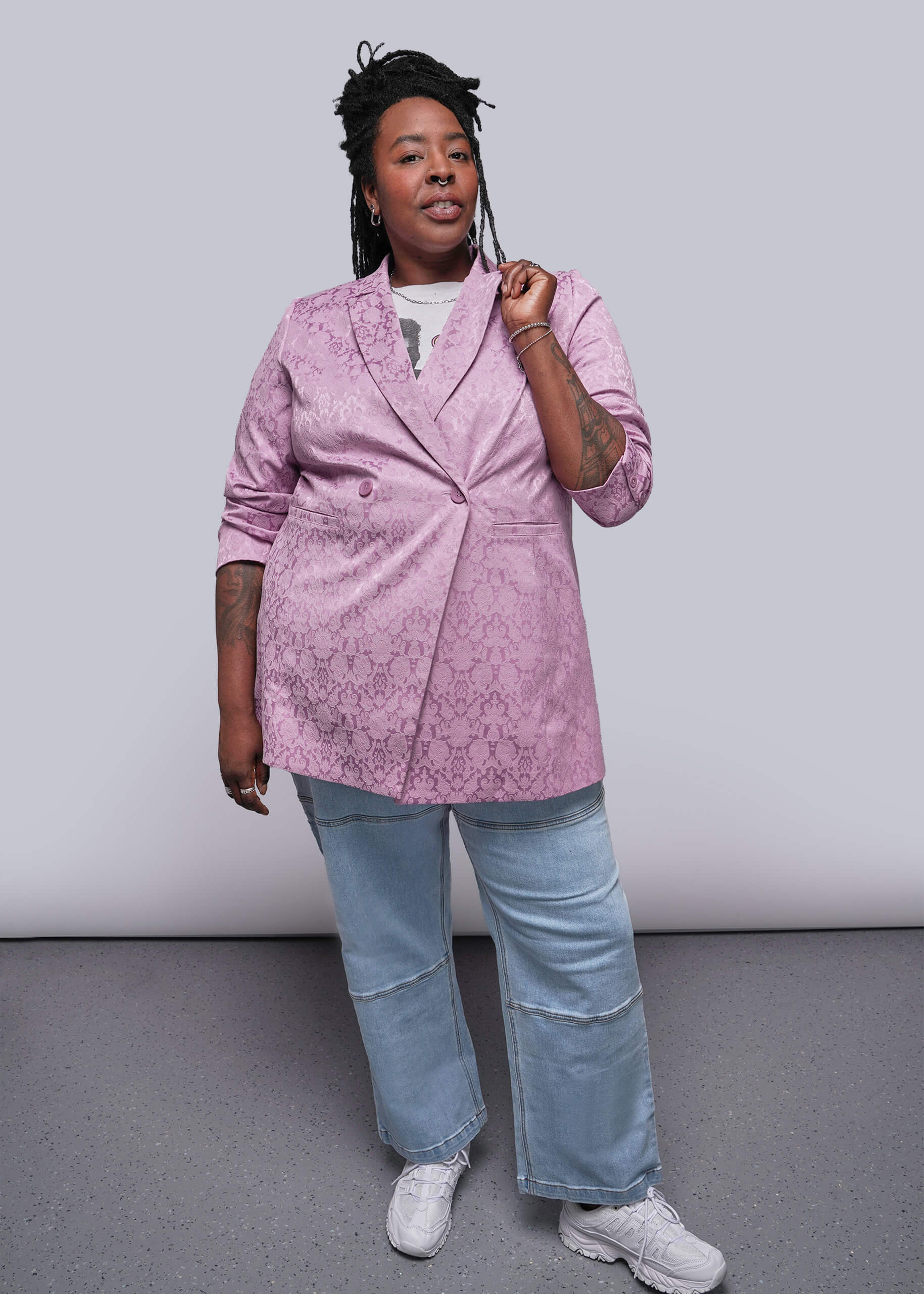 1X=Person wearing a pink blazer with floral pattern, light blue jeans, and white sneakers on a plain background