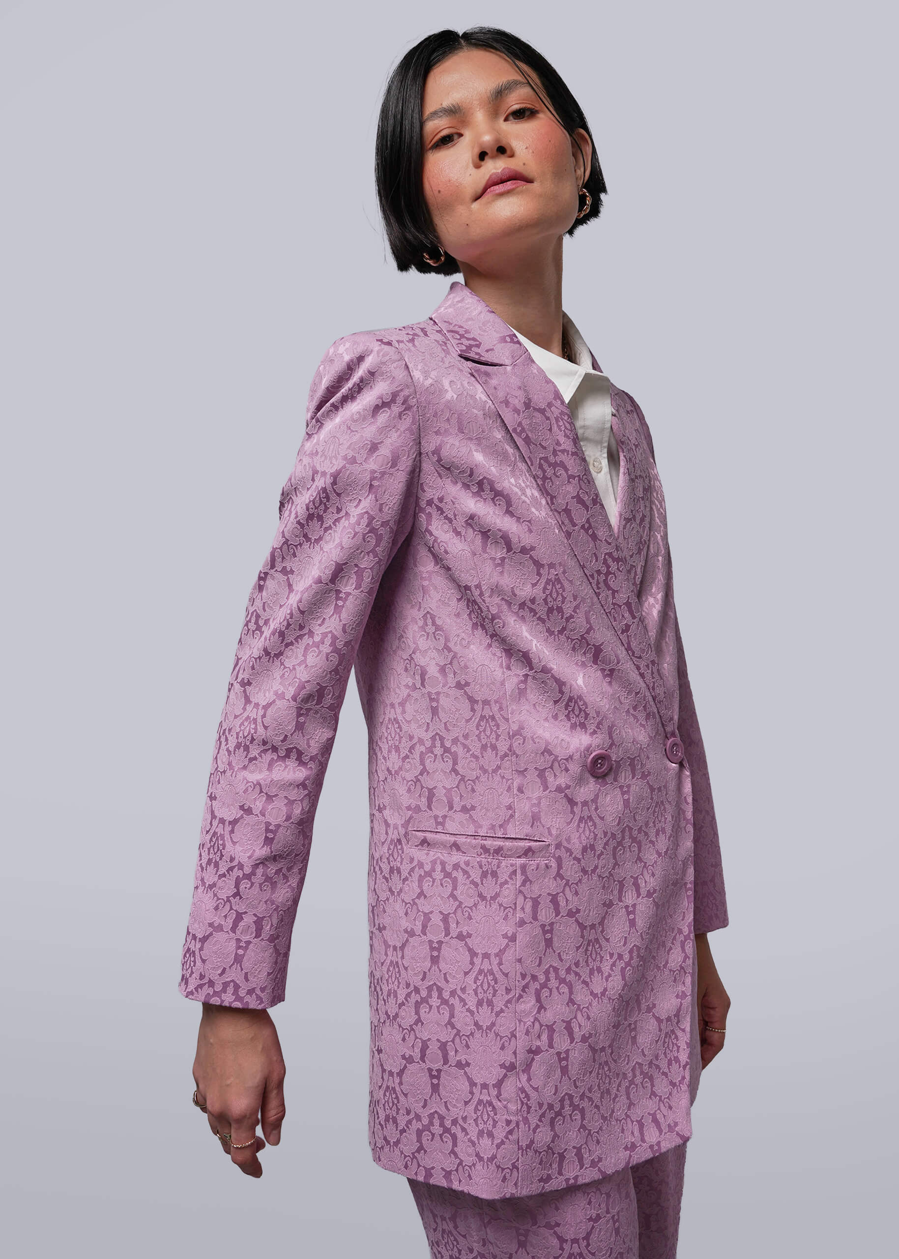 S=Person wearing a pink patterned suit against a plain background