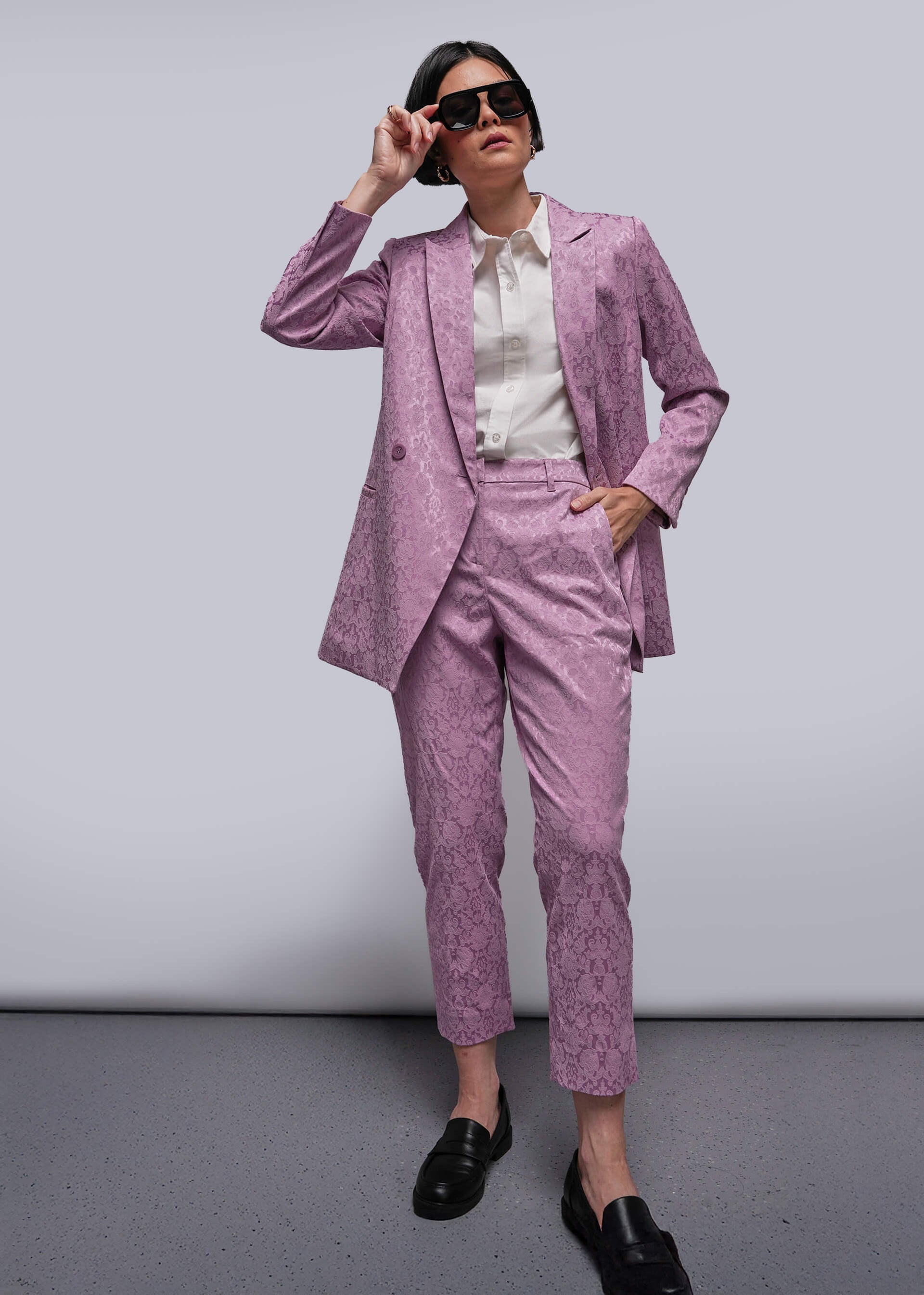 S=Person wearing a pink suit with sunglasses against a plain background