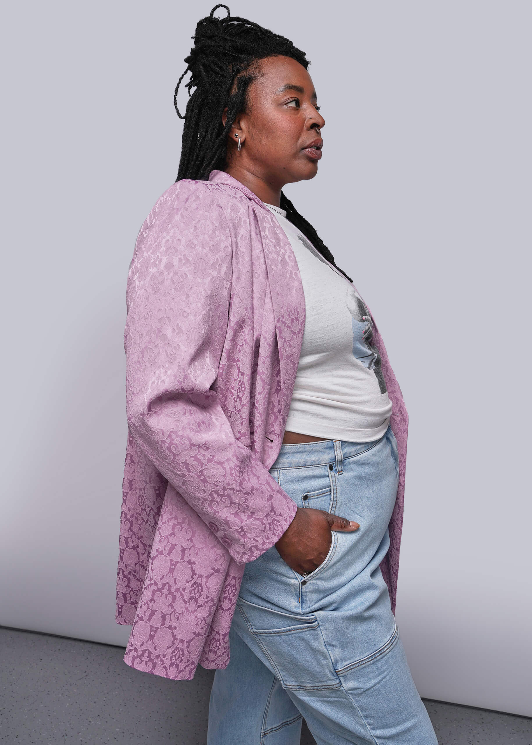 1X=Person wearing a pink jacquard blazer over a white top and blue jeans against a plain background