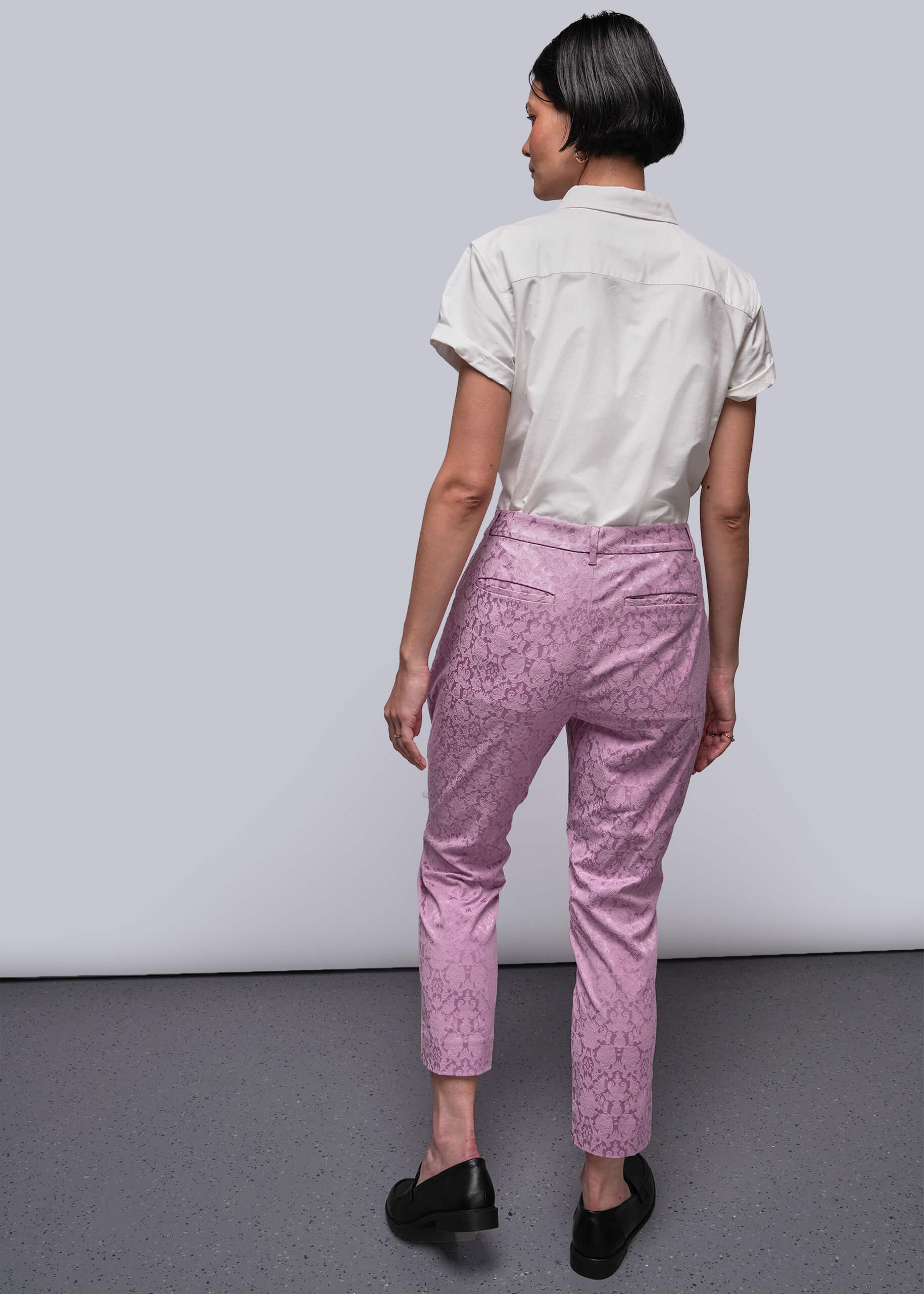 S=Person wearing a light-colored shirt and pink pants against a plain background
