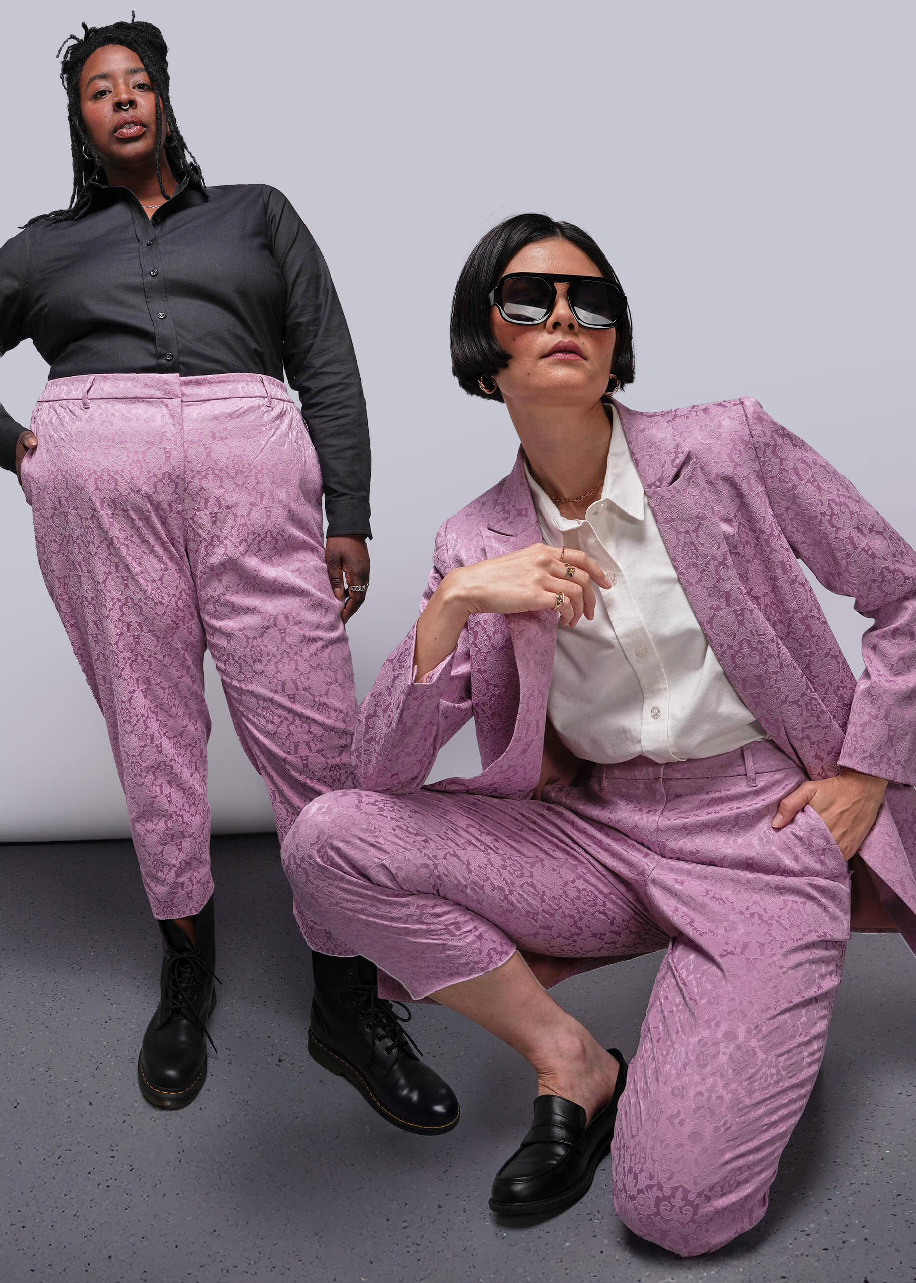 Two people wearing pink suits against a plain background
