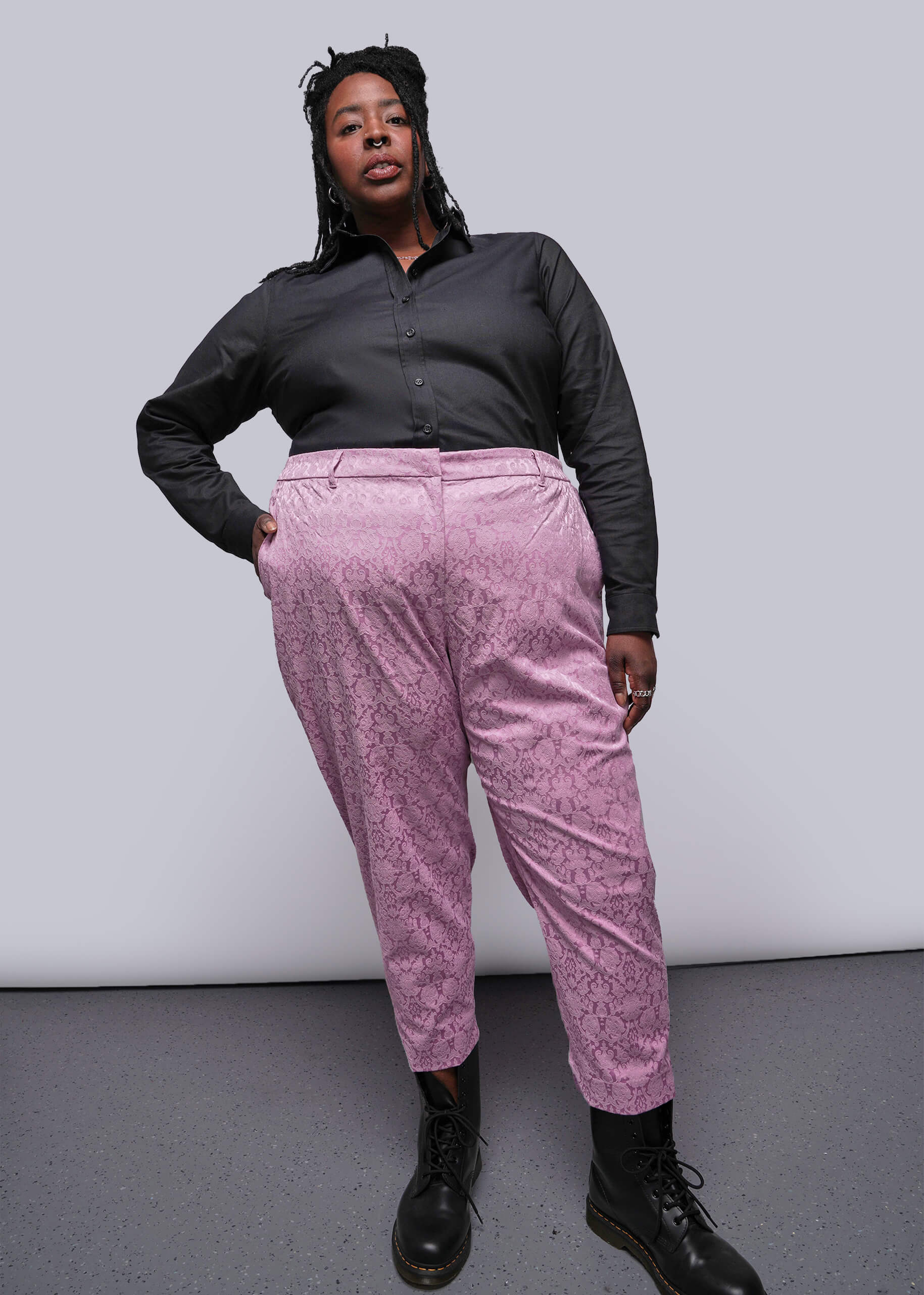 1X=Person wearing a black shirt and pink patterned pants against a plain background
