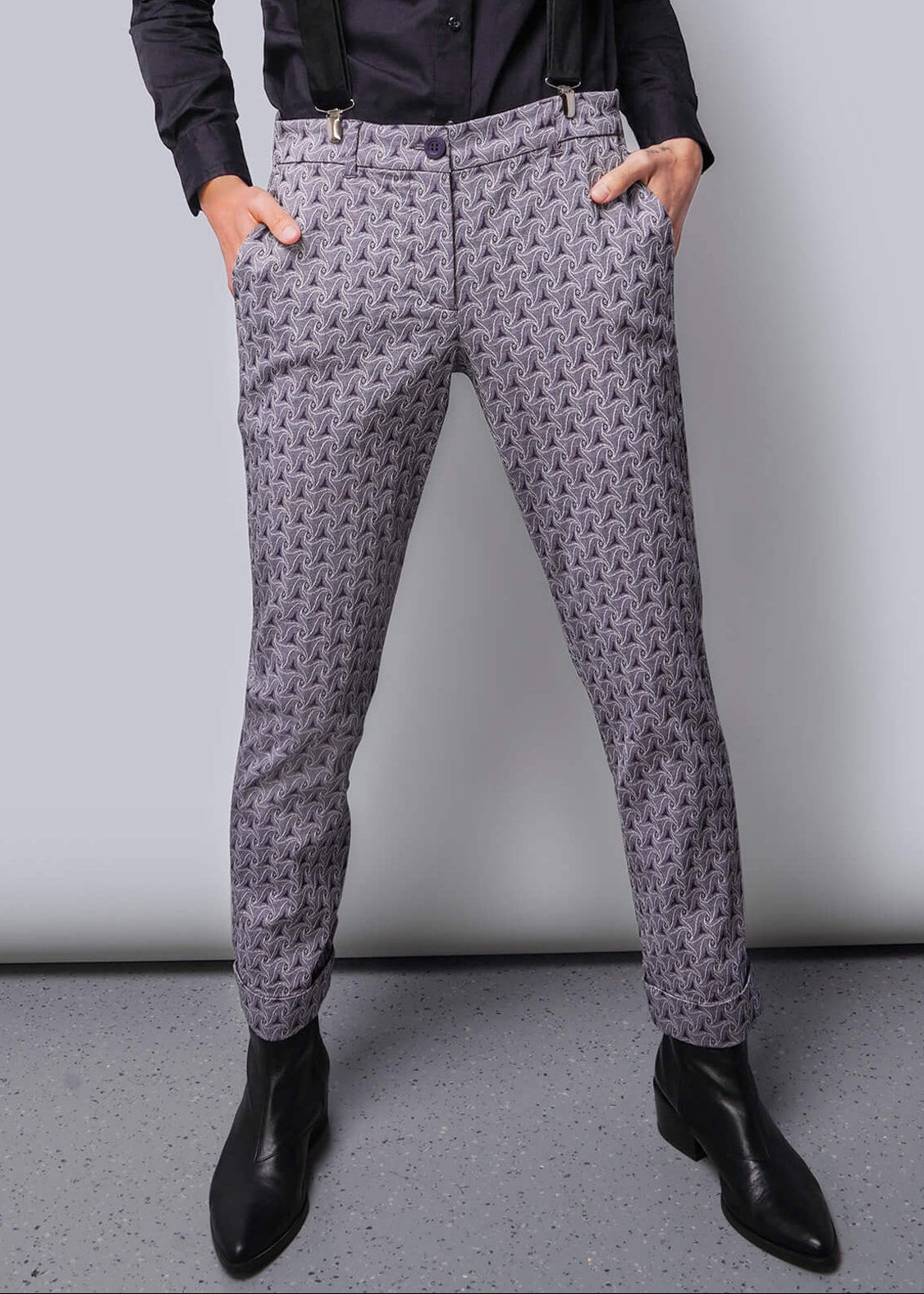 S=Person wearing a dark shirt, suspenders, and patterned pants against a plain background