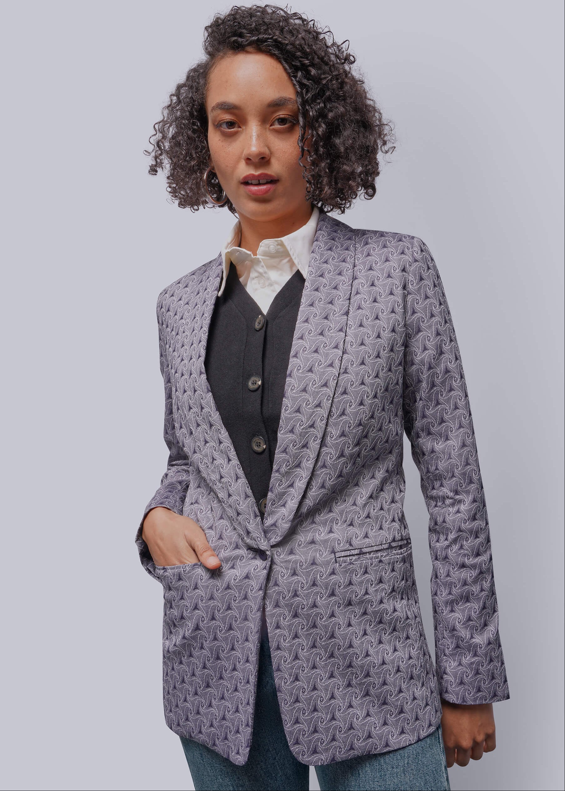 Woman wearing a purple patterned blazer over a shirt and vest on a plain background
