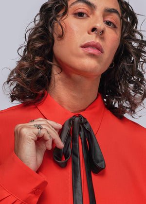 S=Person wearing a red shirt with a black bow tie against a gray background