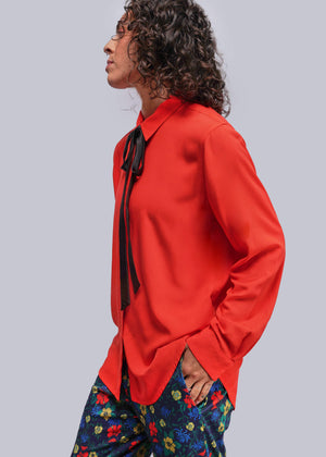 S=Person wearing a bright red shirt with a black tie and colorful pants on a light gray background