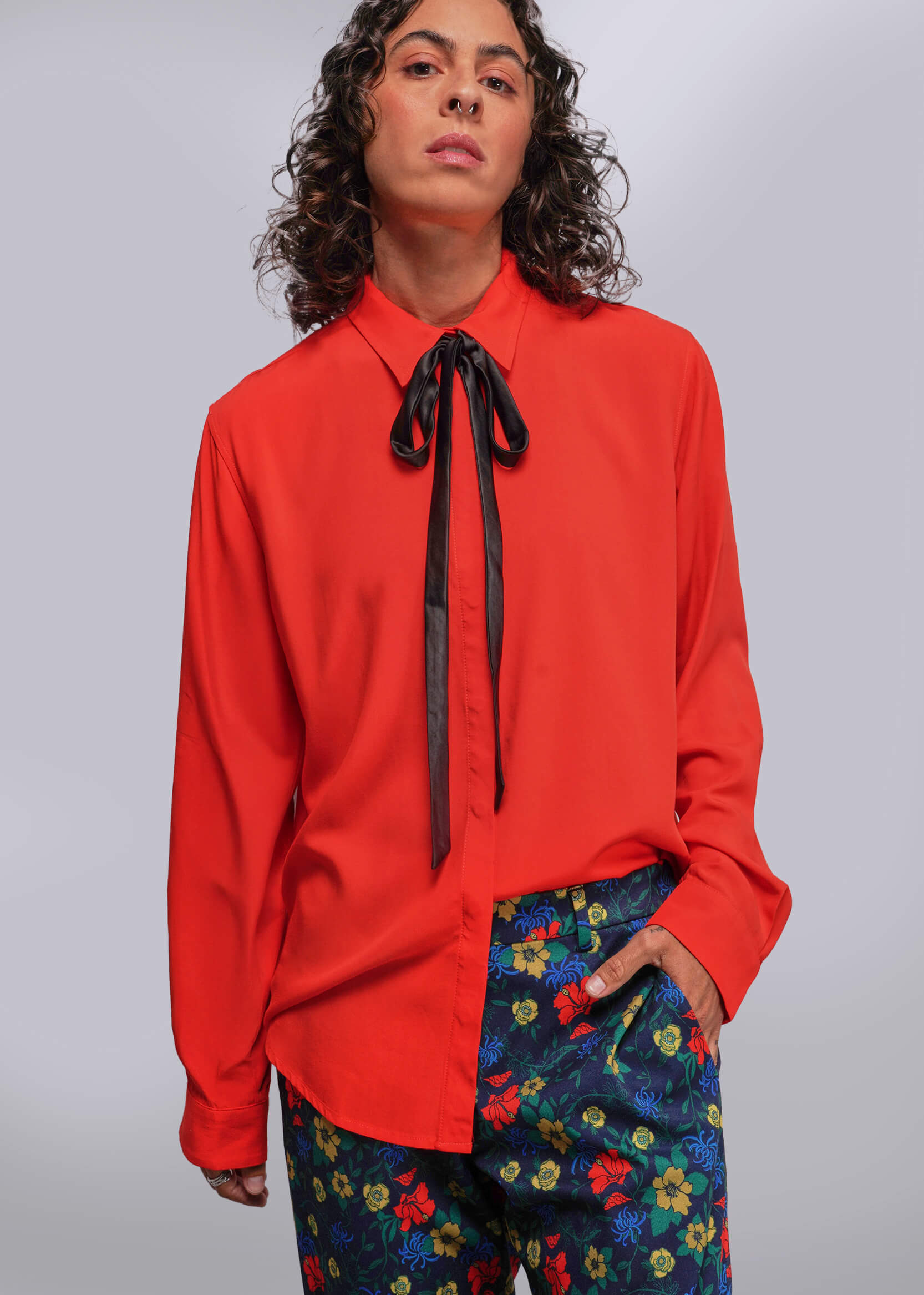 S=Person wearing a red blouse with a black ribbon and colorful pants on a gray background