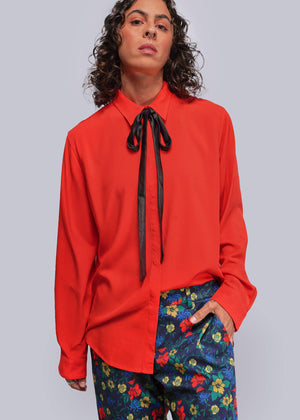 S=Person wearing a red blouse with a black ribbon and colorful pants on a gray background