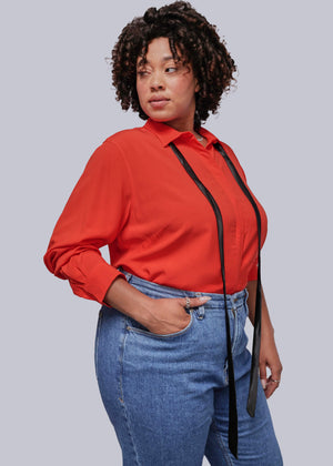 1X=Person wearing a red blouse with a black ribbon and blue jeans on a plain background