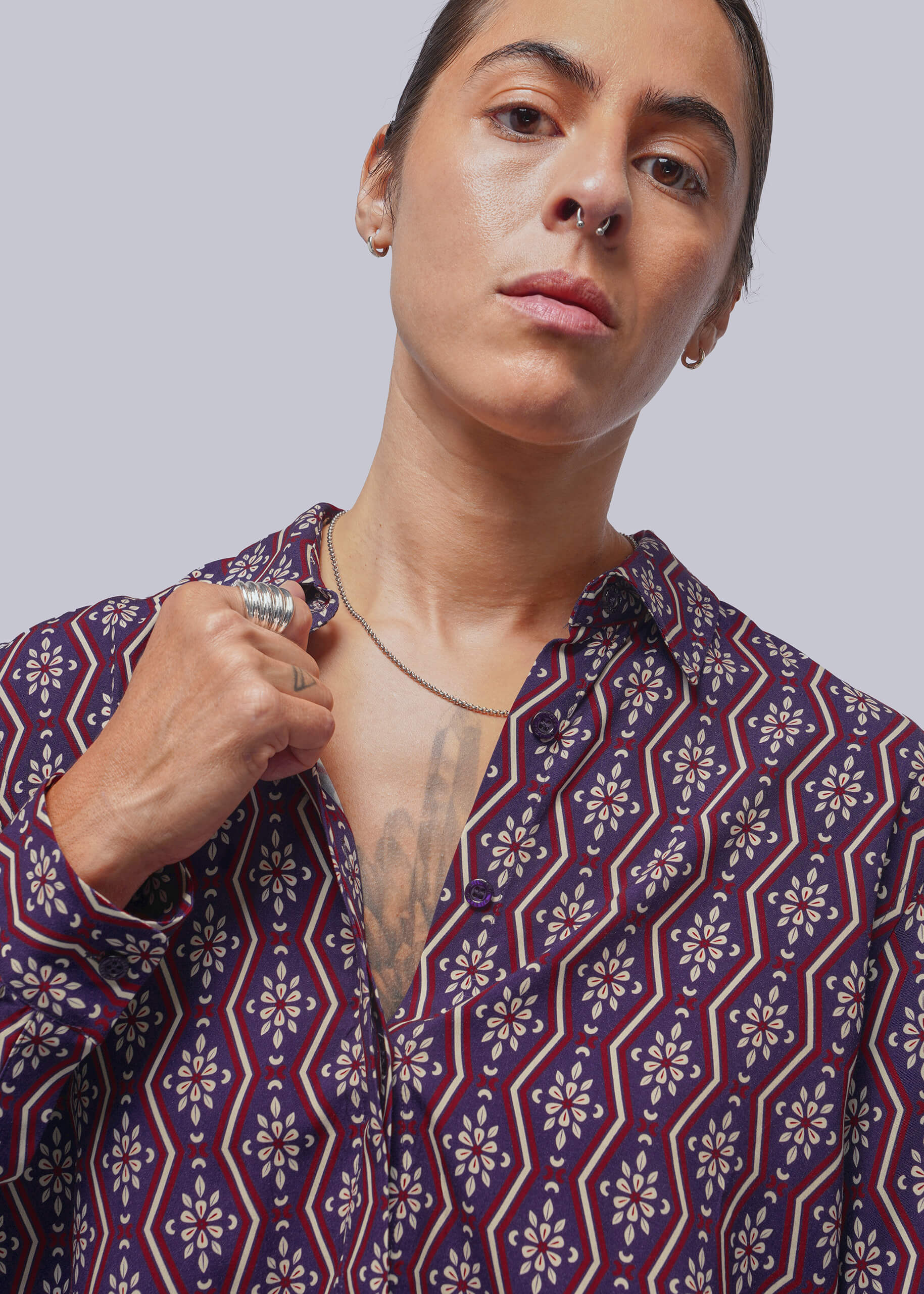 A close-up of a person wearing a patterned button-up shirt with a geometric and floral design in navy blue, red, and white, set against a solid light gray background.
