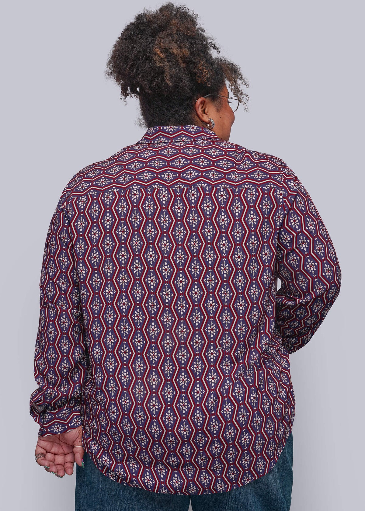 1X=A person shown from the back wearing a long-sleeve button-up shirt with a red, blue, and white geometric pattern, paired with blue jeans, against a solid gray background.