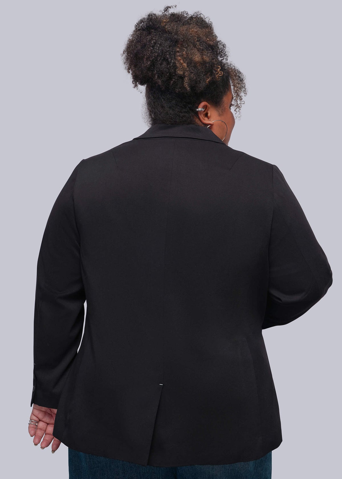 1X=A person shown from the back wearing a black blazer and blue jeans against a plain light gray studio background.