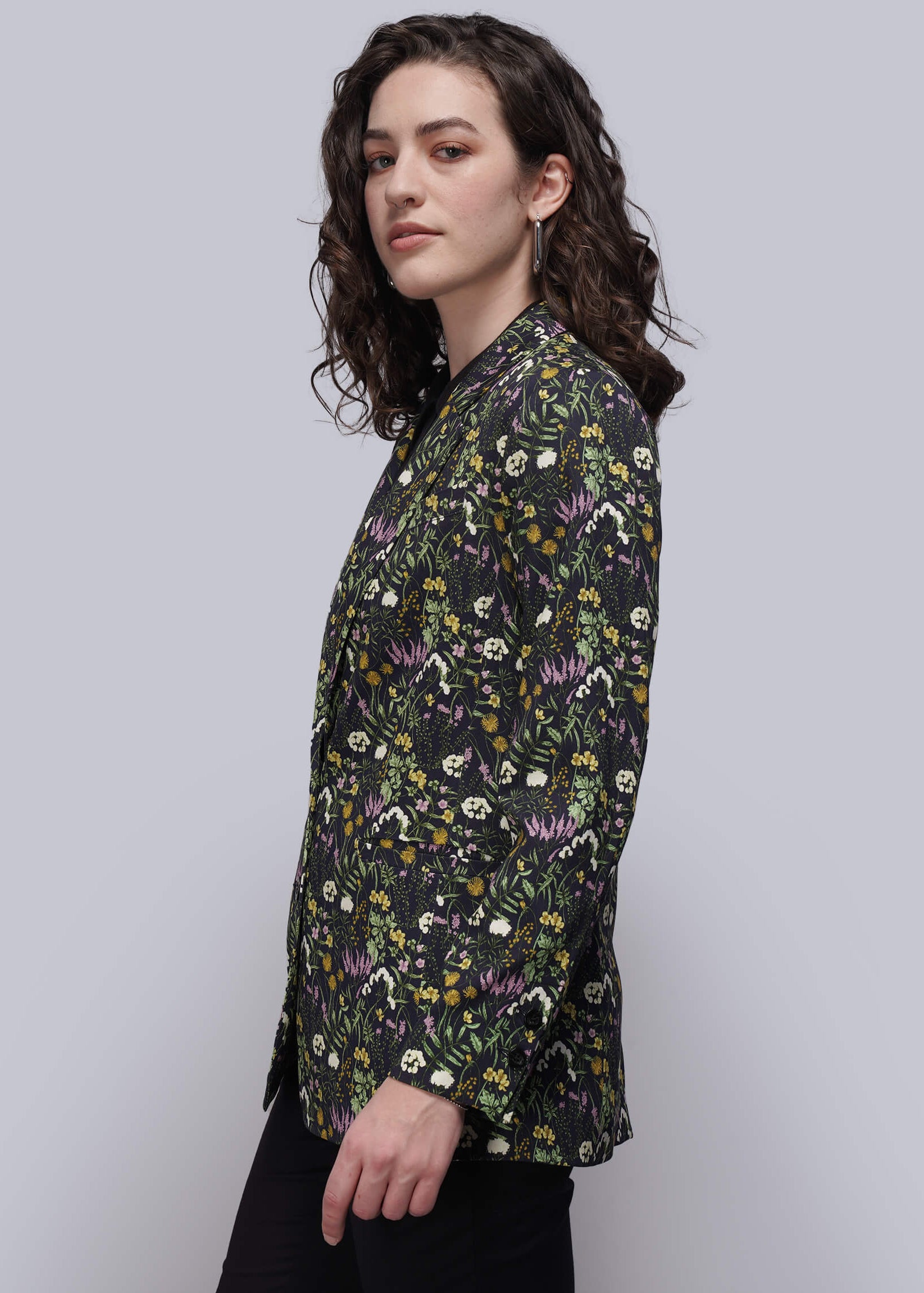 S=Woman wearing a dark floral patterned blazer against a plain background