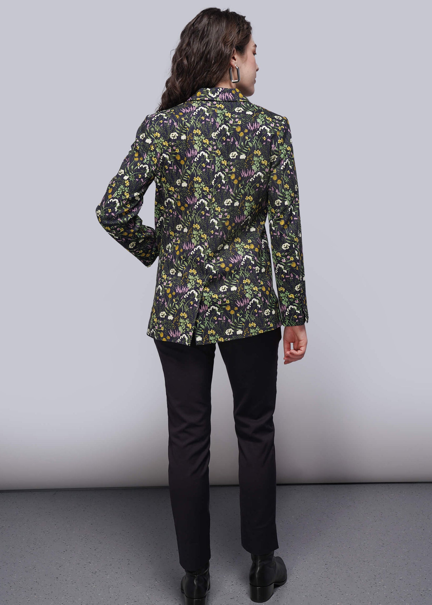S=Person wearing a floral patterned jacket and black pants on a plain background