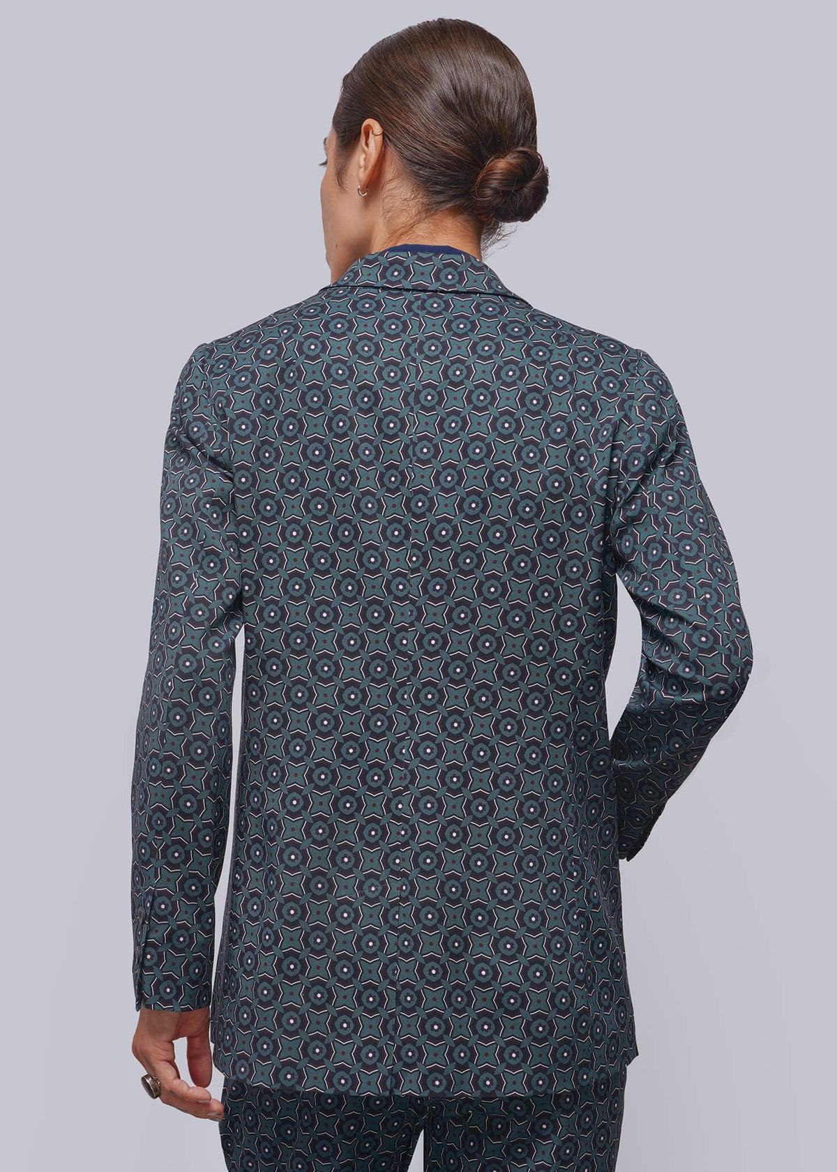 S=A person viewed from the back wearing a dark slate blue patterned suit with a matching blazer and trousers. The fabric features a repeating circular medallion pattern in lighter blue and white.