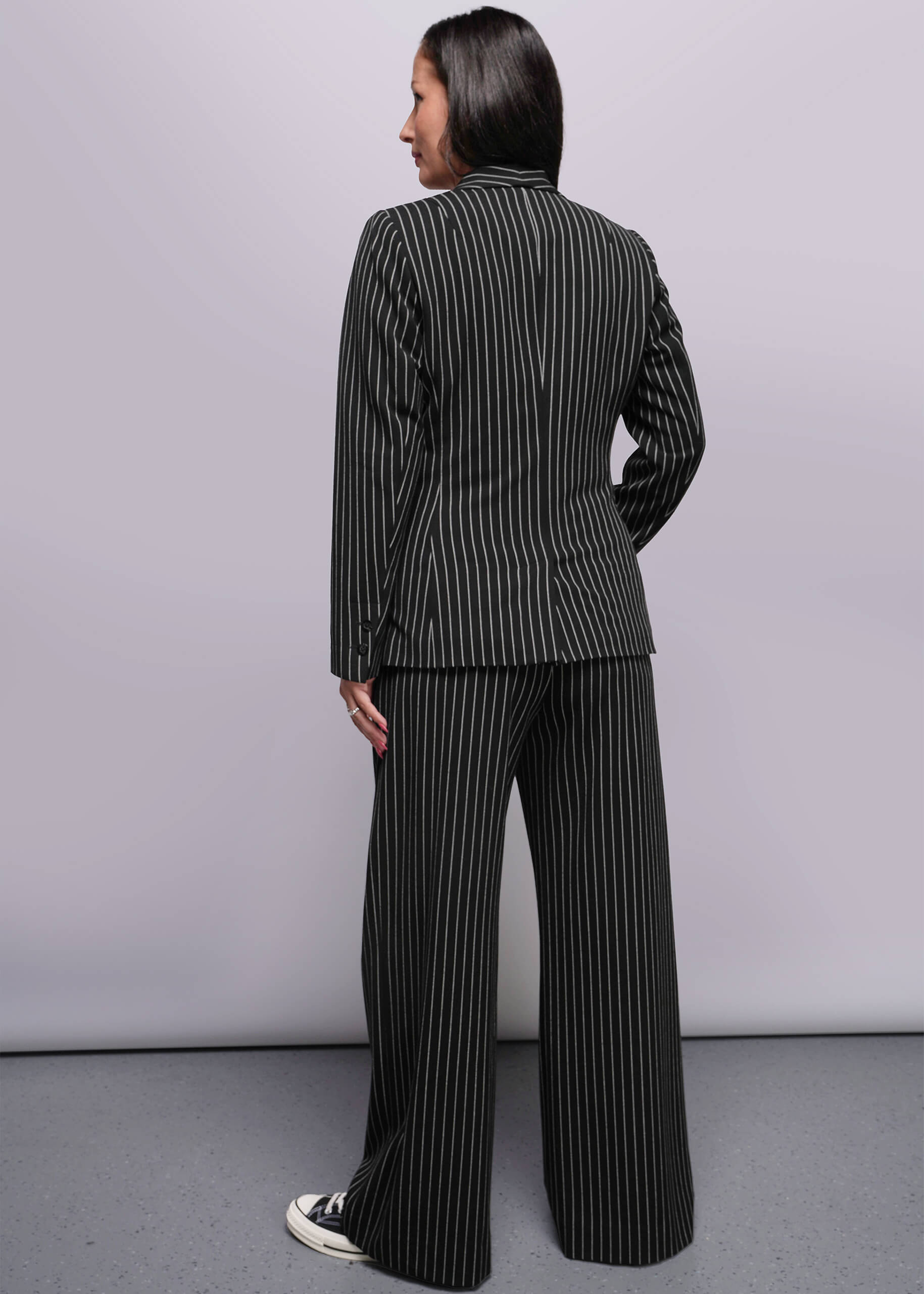 S=Person wearing a black and white pinstripe suit standing against a plain background