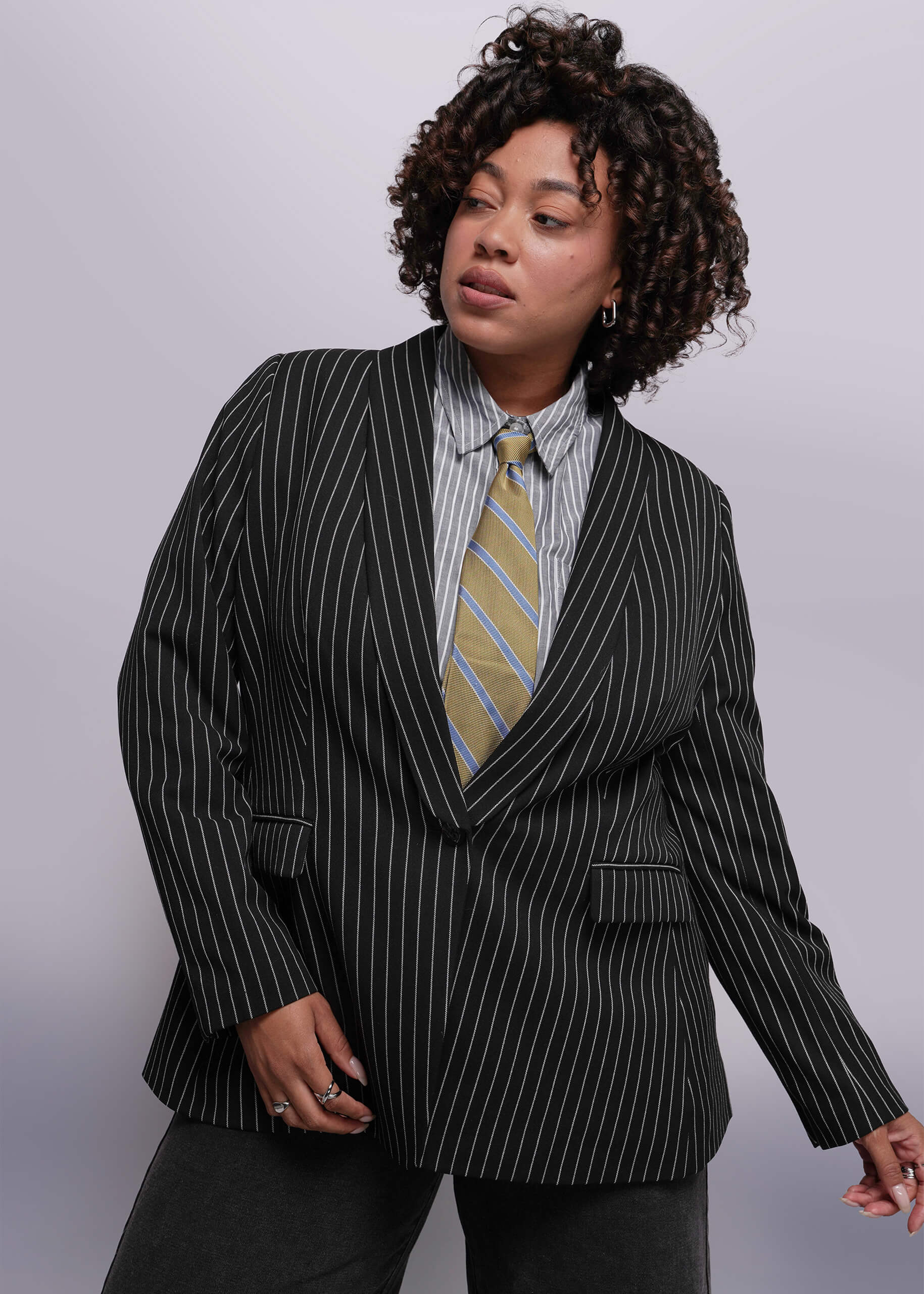1X=Person wearing a black pinstripe suit with a striped tie against a plain background