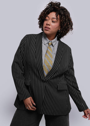 1X=Person wearing a black pinstripe suit with a striped tie against a plain background