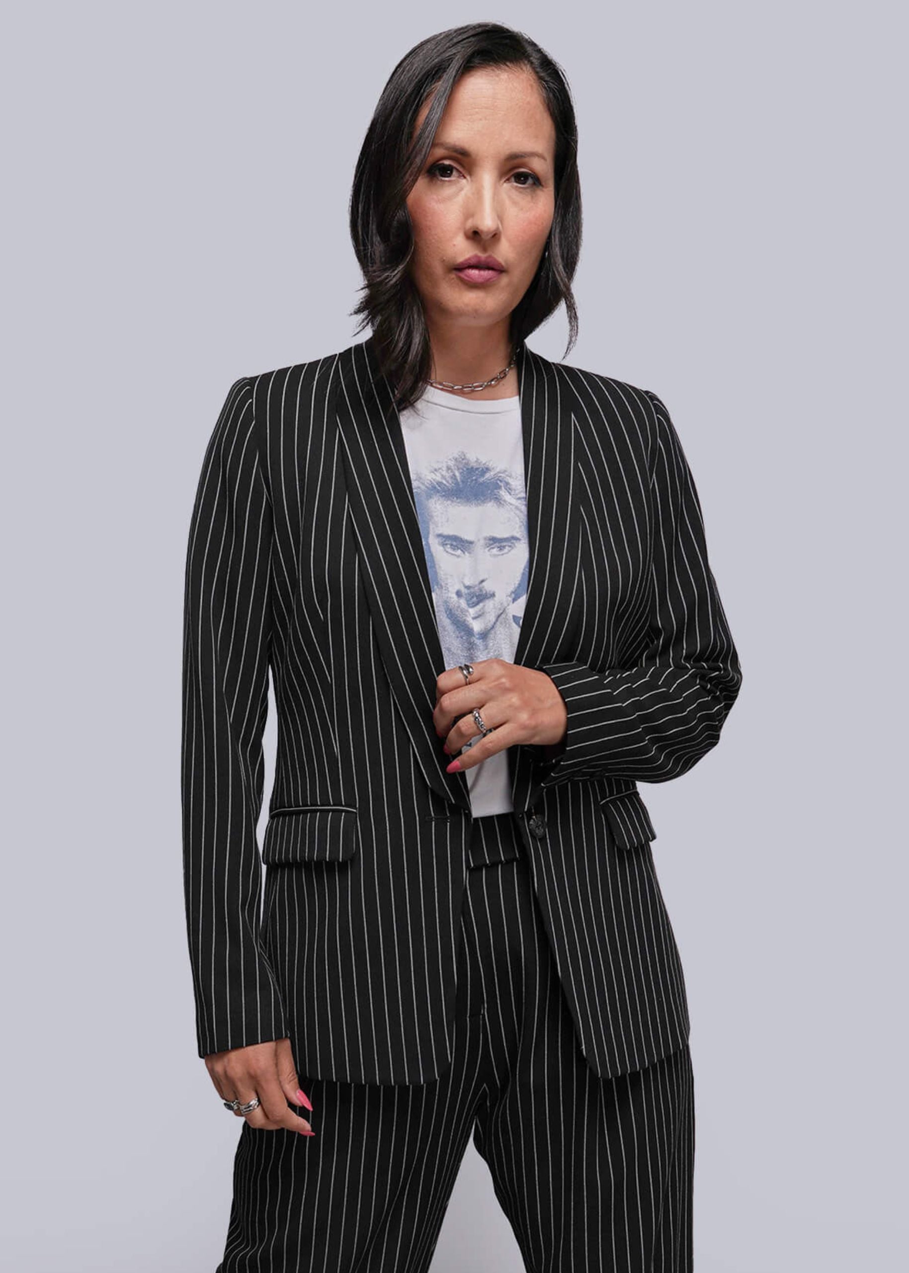 S=Woman wearing a black pinstripe suit over a light blue graphic t-shirt on a gray background