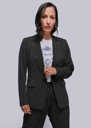 S=Woman wearing a black pinstripe suit over a light blue graphic t-shirt on a gray background