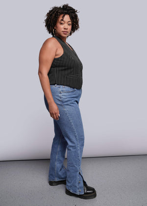 1X=Woman wearing a black sleeveless top and blue jeans against a plain background