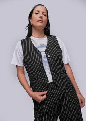 1X=Woman wearing a black pinstripe vest over a white t-shirt with a graphic design on a plain background