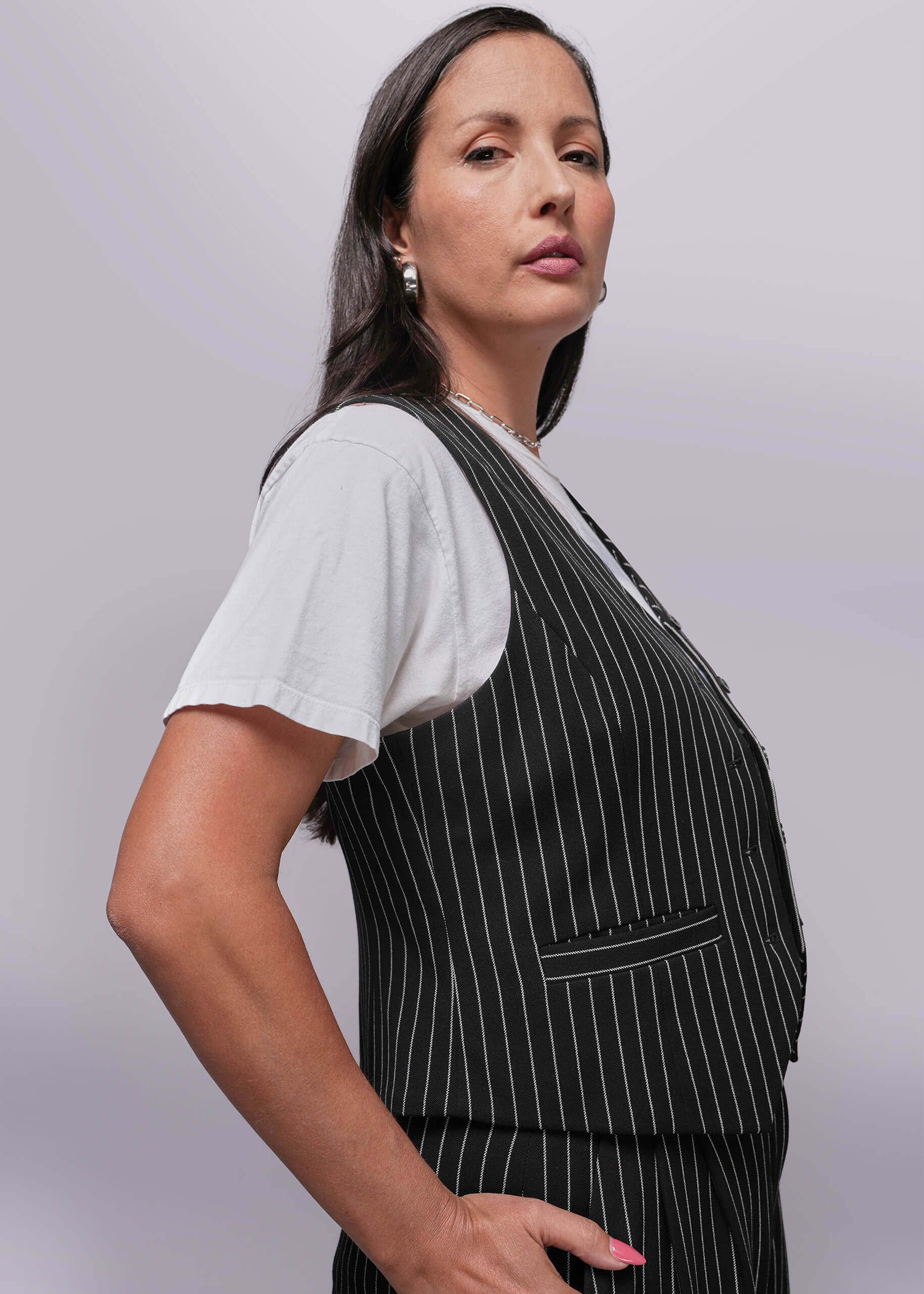 1X=Woman wearing a black pinstripe apron over a white shirt on a light gray background